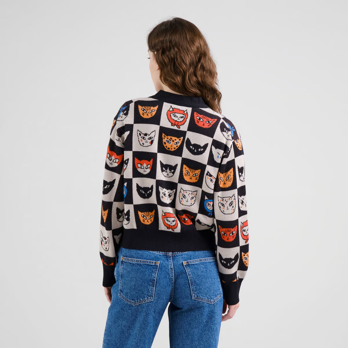 Gestrickter, geknöpfter Cardigan mit schwarz-weiss Schachbrettmuster und in jedem Feld ist ein leiner Katzenkopf in orange-rot.