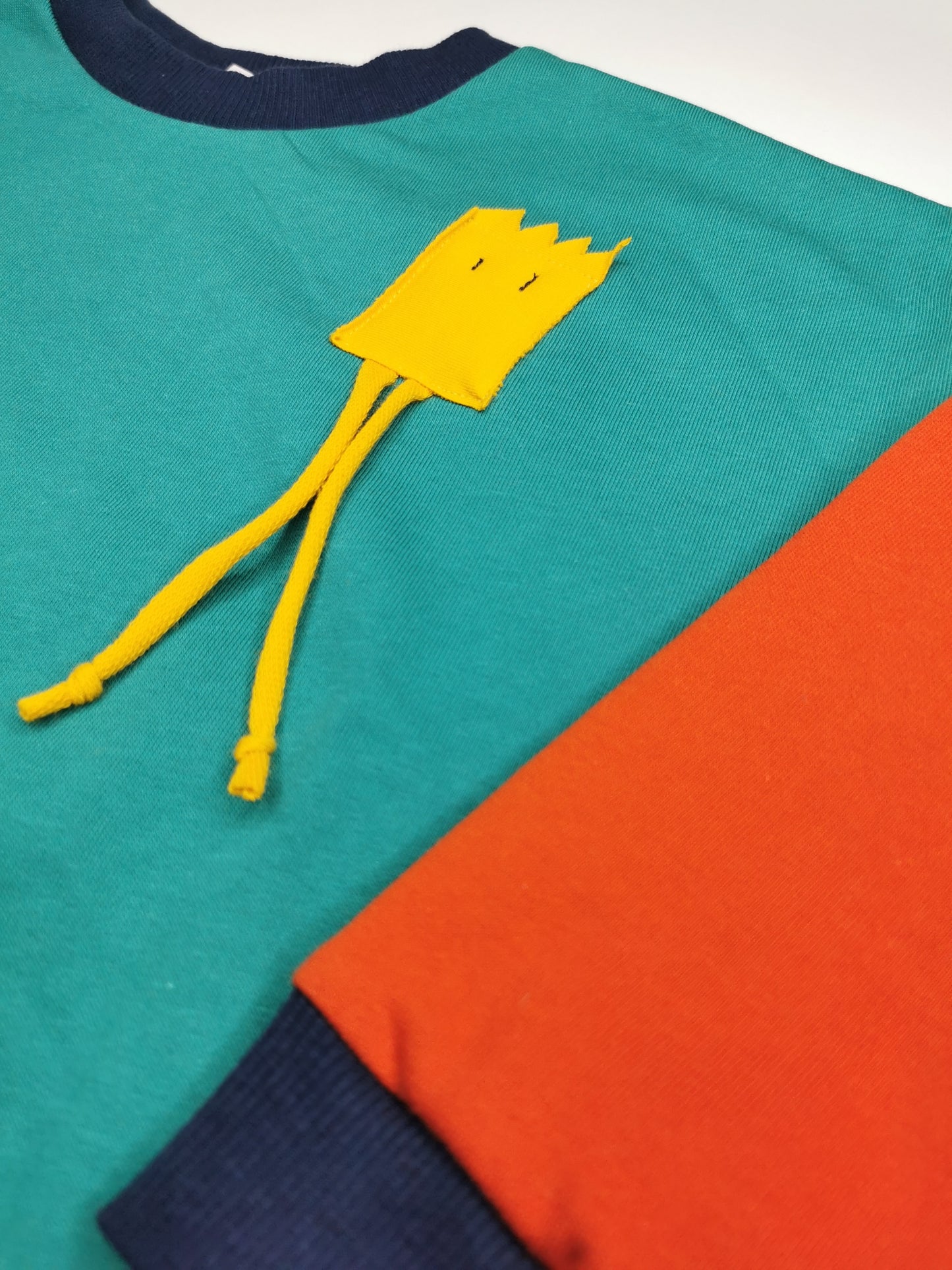 Lustiges, gelbes Strahlemännchen auf türkis orange Sweatshrt mit dunkelblauen Bündchen.