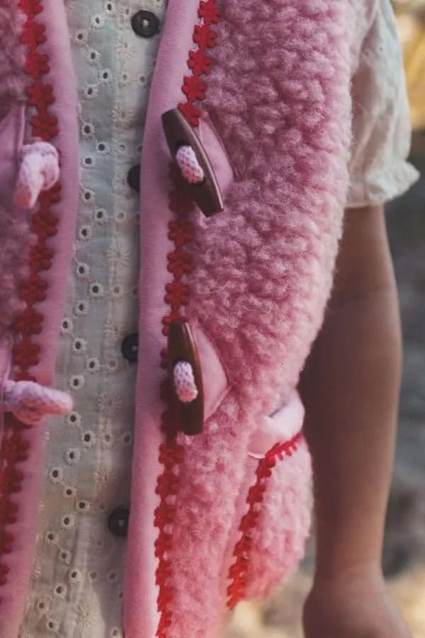 Weiche Kinderweste aus Teddyplüsch in reiner Wolle, pink mit roter Blumenbordüre als Akzent.