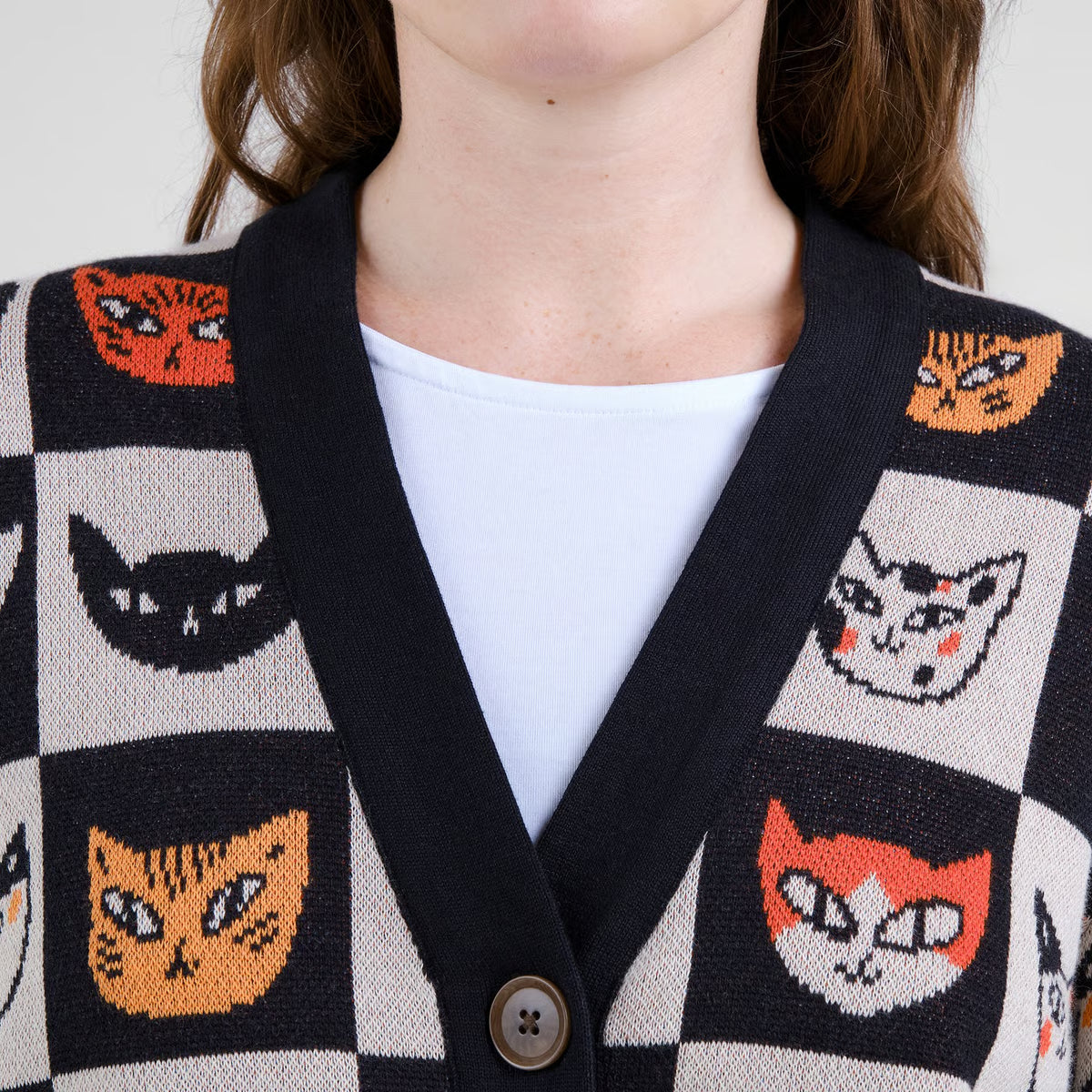Gestrickter, geknöpfter Cardigan mit schwarz-weiss Schachbrettmuster und in jedem Feld ist ein leiner Katzenkopf in orange-rot.
