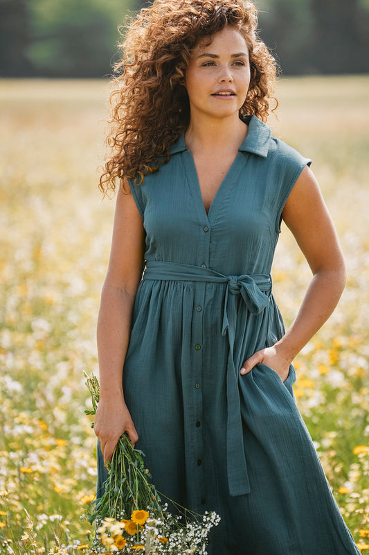 Kleid mit Kragen und frontaler Knöpfung, Bindegürtel und seitliche Eingrifftaschen in Petrol, das Kleid ist wadenlang und ärmellos.