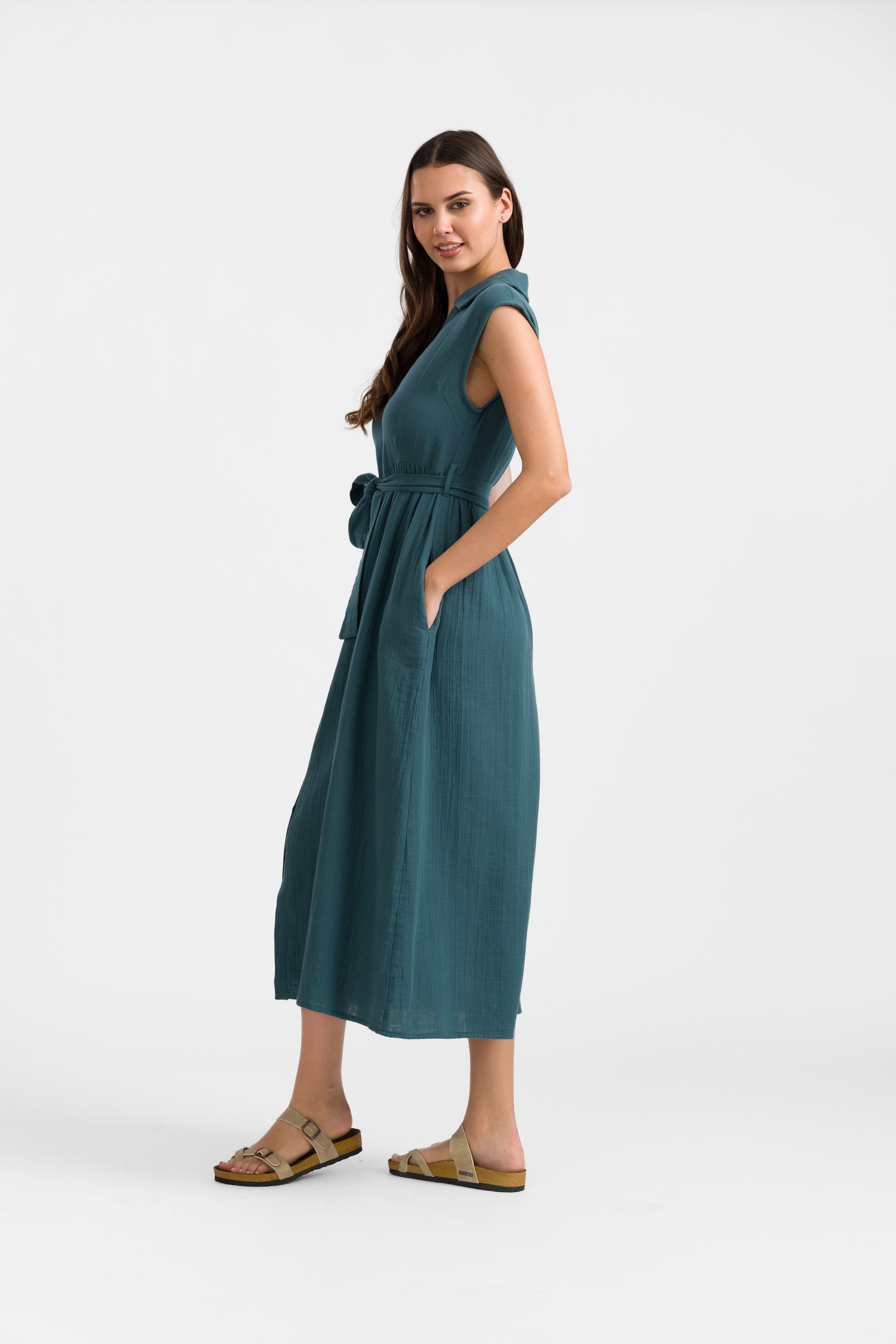 Kleid mit Kragen und frontaler Knöpfung, Bindegürtel und seitliche Eingrifftaschen in Petrol, das Kleid ist wadenlang und ärmellos.