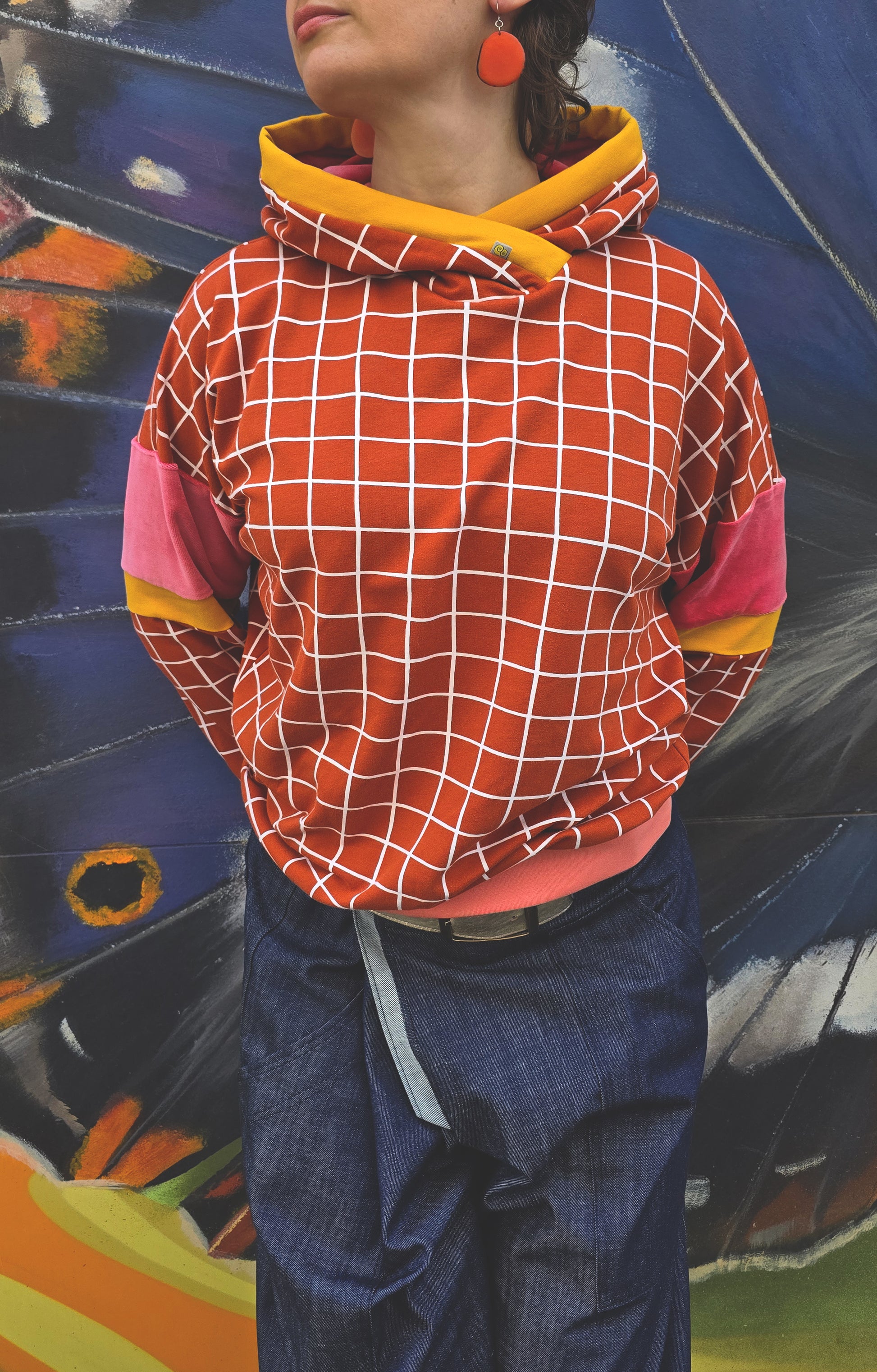 Kapuzen Sweatshirt mit GridMuster in orange und weiss, die Kapuze hat einen Gelbakzent und innen ist sie aus pink Nicky, Bündchen sind apricot.