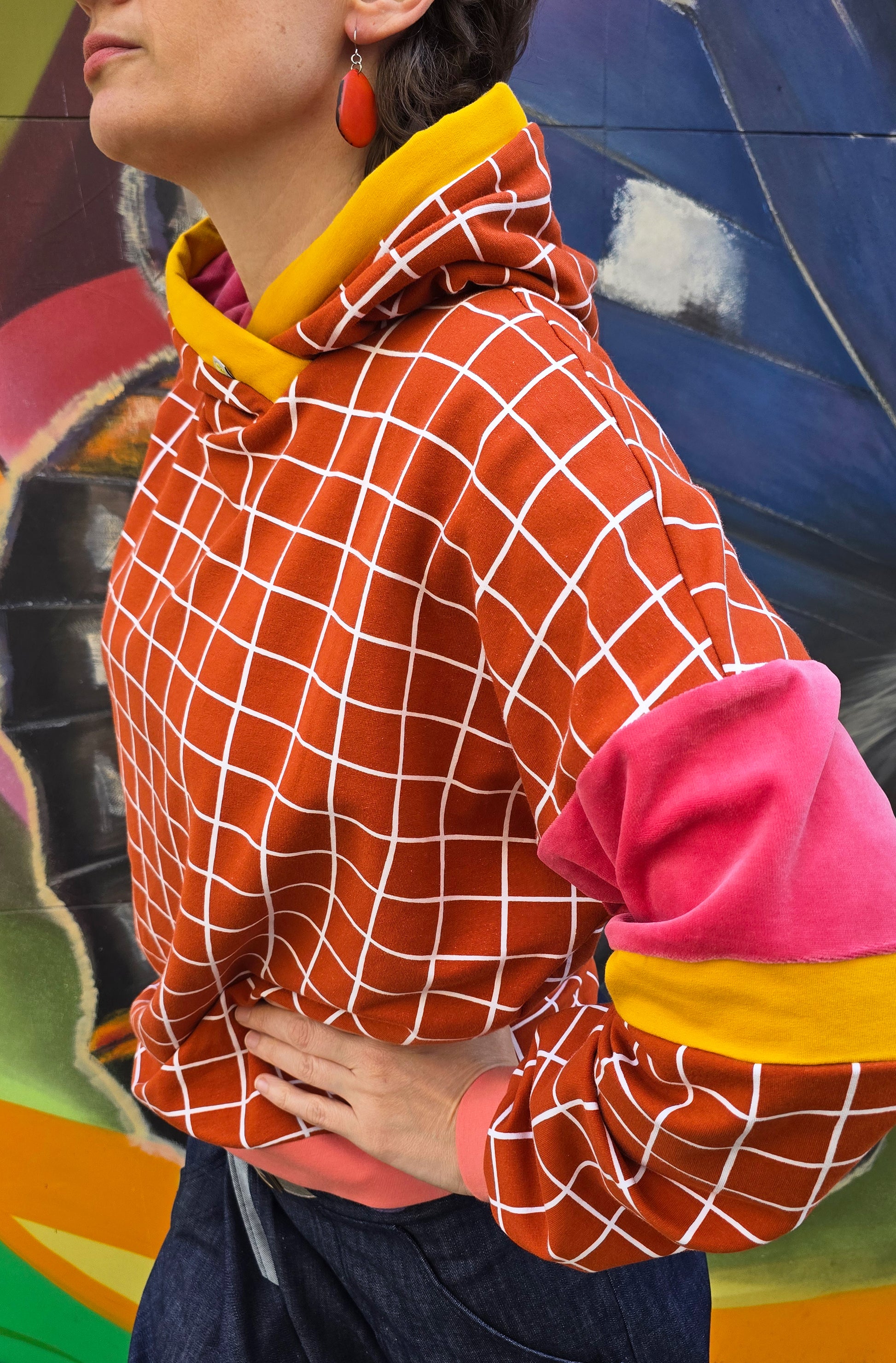 Kapuzen Sweatshirt mit GridMuster in orange und weiss, die Kapuze hat einen Gelbakzent und innen ist sie aus pink Nicky, Bündchen sind apricot.