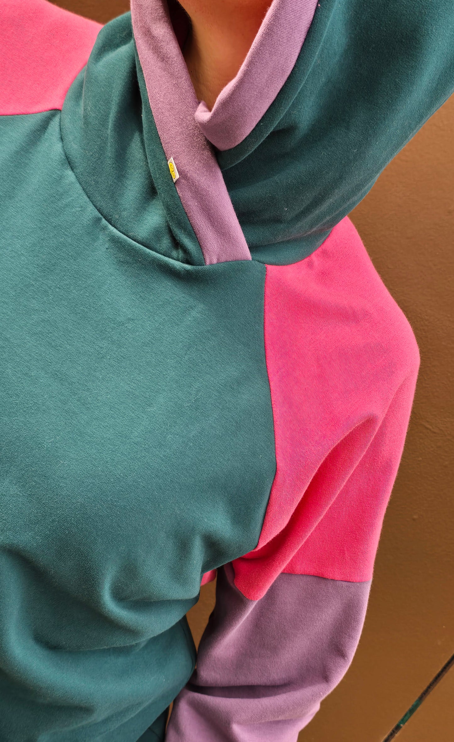 Kapuzenpullover aus Sweat Jersey in colourblock petrol, pink und lila mit mint Bünchen und Kapuzeninnenteil in Pink mit Borte in Lila.