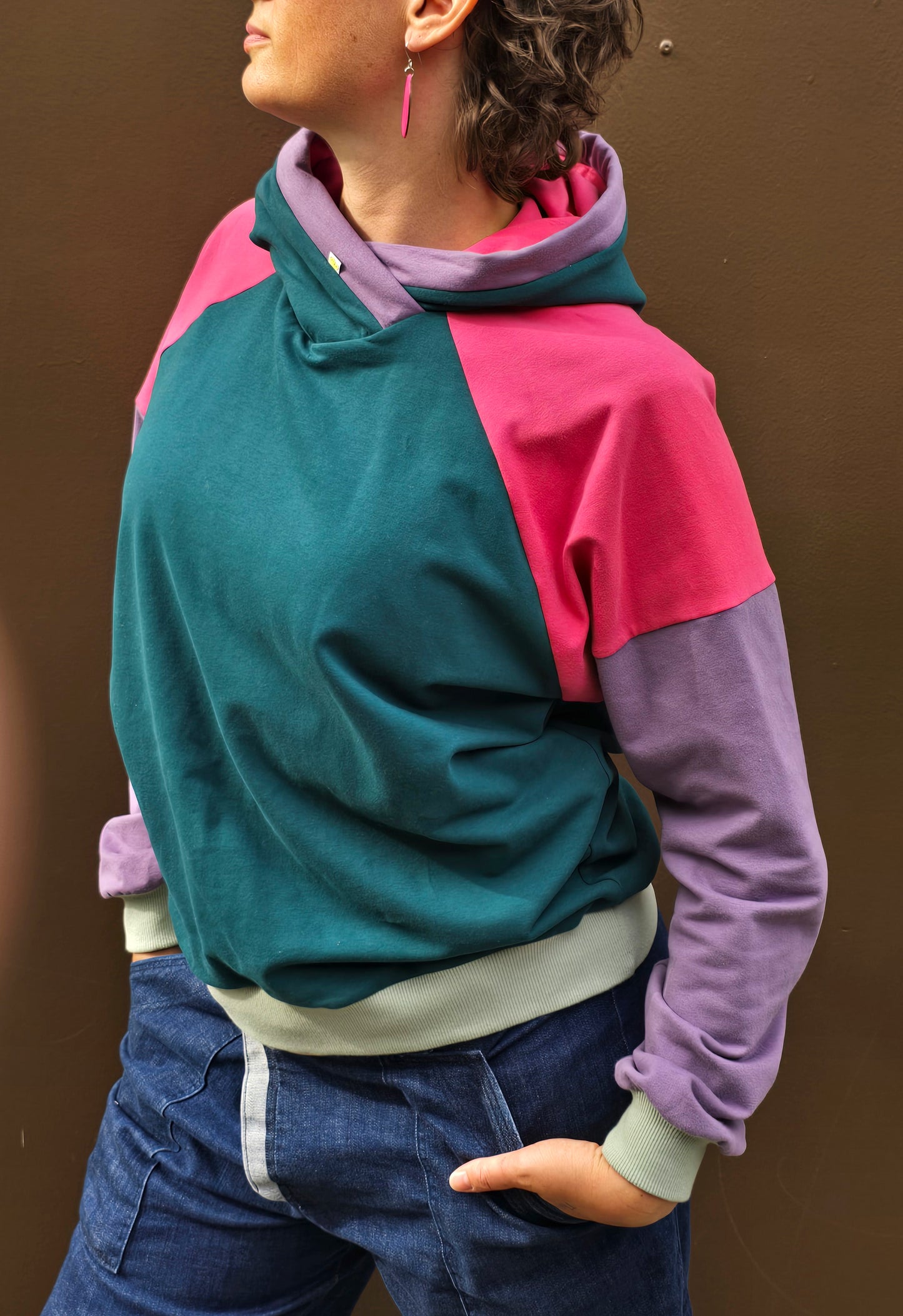 Kapuzenpullover aus Sweat Jersey in colourblock petrol, pink und lila mit mint Bünchen und Kapuzeninnenteil in Pink mit Borte in Lila.