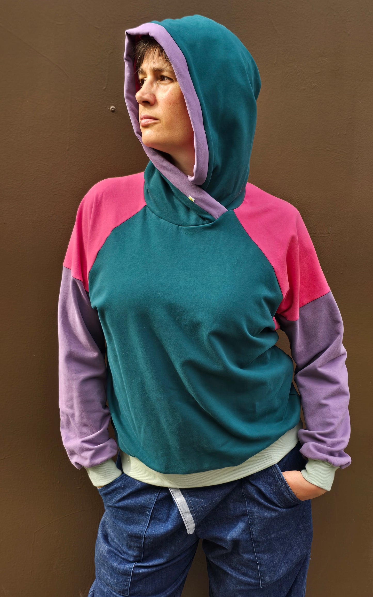 Kapuzenpullover aus Sweat Jersey in colourblock petrol, pink und lila mit mint Bünchen und Kapuzeninnenteil in Pink mit Borte in Lila.