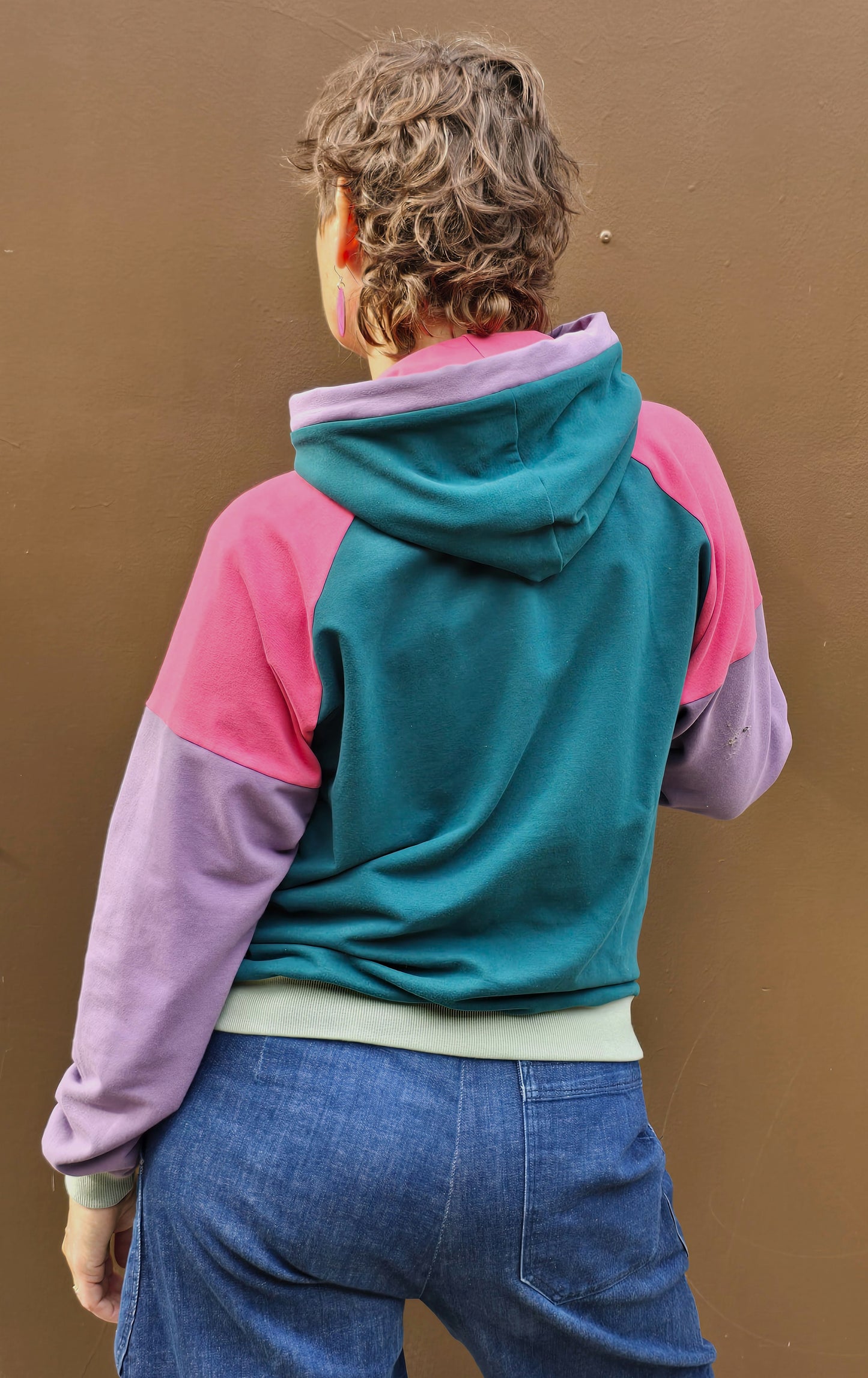Kapuzenpullover aus Sweat Jersey in colourblock petrol, pink und lila mit mint Bünchen und Kapuzeninnenteil in Pink mit Borte in Lila.