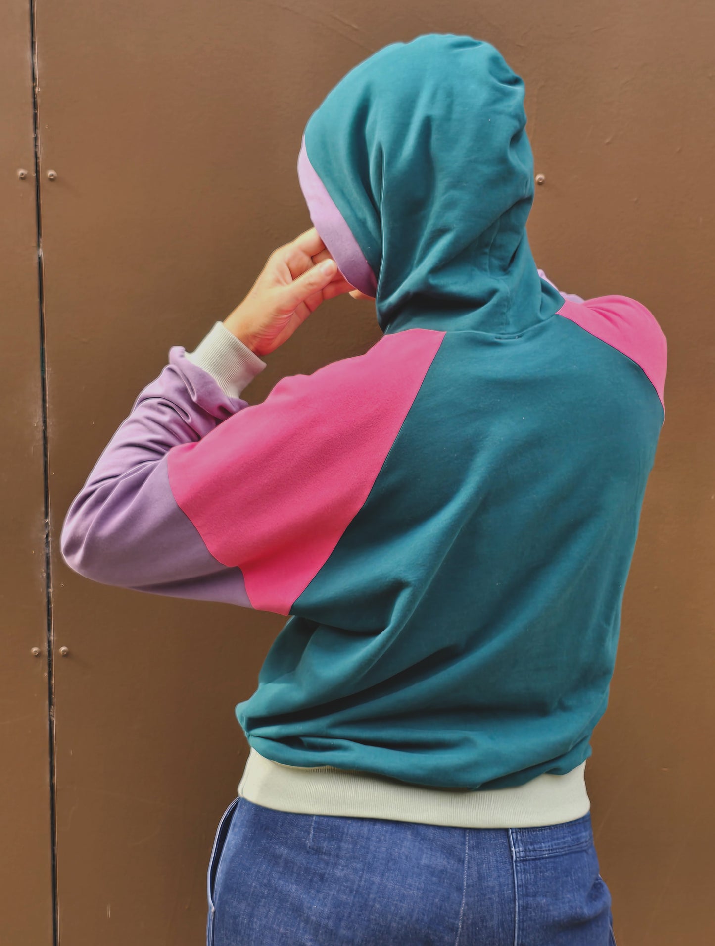 Kapuzenpullover aus Sweat Jersey in colourblock petrol, pink und lila mit mint Bünchen und Kapuzeninnenteil in Pink mit Borte in Lila.