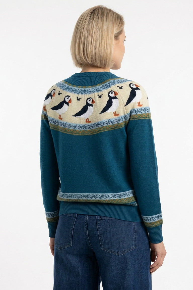 Gestrickter Pullover aus petrol farbener Biobaumwolle im Fairsle Stil mit rundlaufendem Papageientaucher Muster in orange, schwarz und weiss, an den Ärmeln gibt es ebenfalls eine kleinere Borte im abgestimmten Streifen und Zackenmuster.