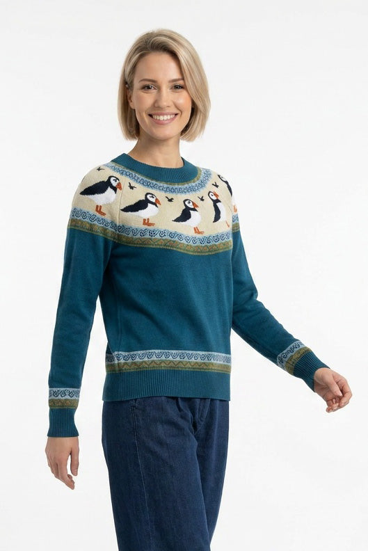 Gestrickter Pullover aus petrol farbener Biobaumwolle im Fairsle Stil mit rundlaufendem Papageientaucher Muster in orange, schwarz und weiss, an den Ärmeln gibt es ebenfalls eine kleinere Borte im abgestimmten Streifen und Zackenmuster.