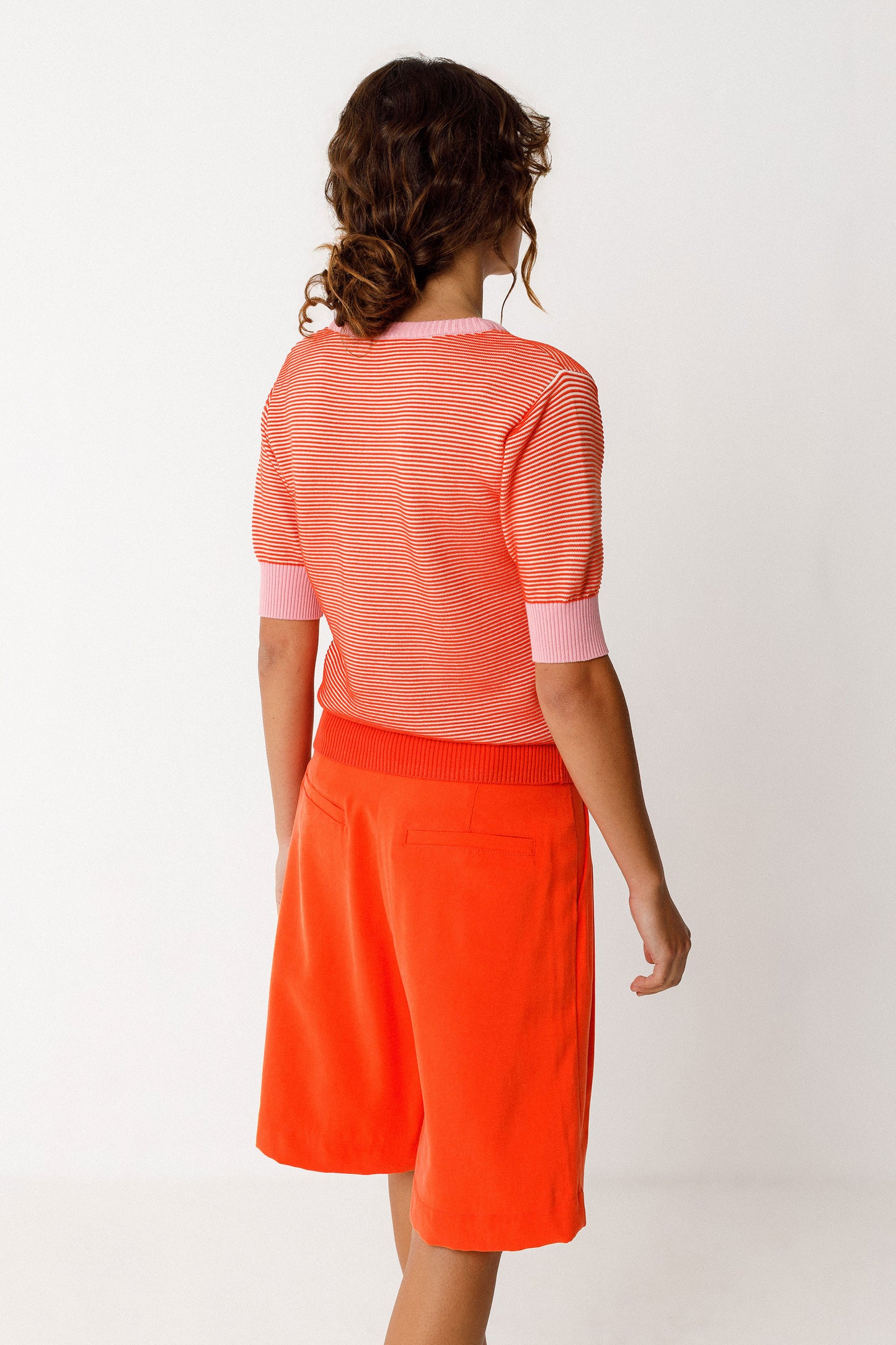 Kurzärmliges Damen Stricktop in Streifenoptik orange und rosa, mit rosa Armbündchen und Halsabschuss.