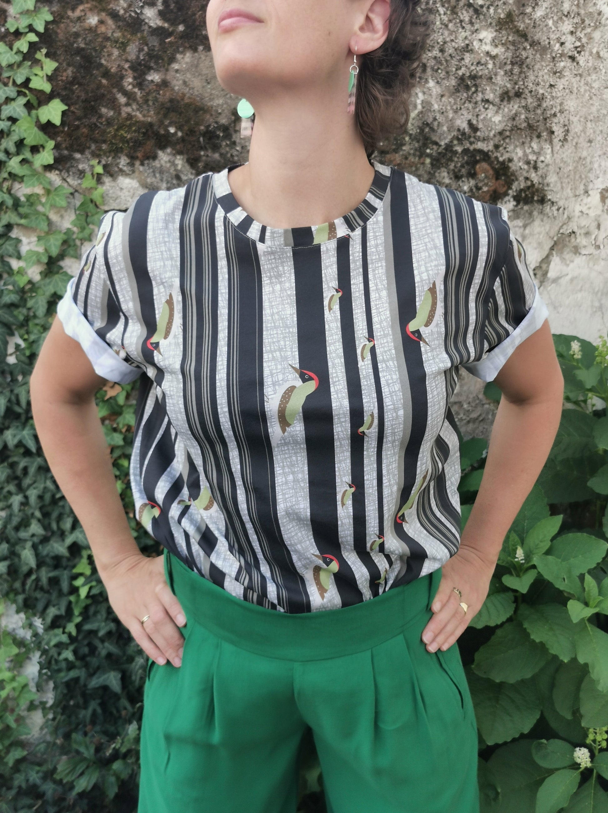 T-Shirt aus Biobaumwolle mit Streifenmuster in unregelmäßigen Abständen- die Streifen sind schwarz auf weiß und ein Grünspecht pickt Löcher in die Streifen, witzig, verspielt.