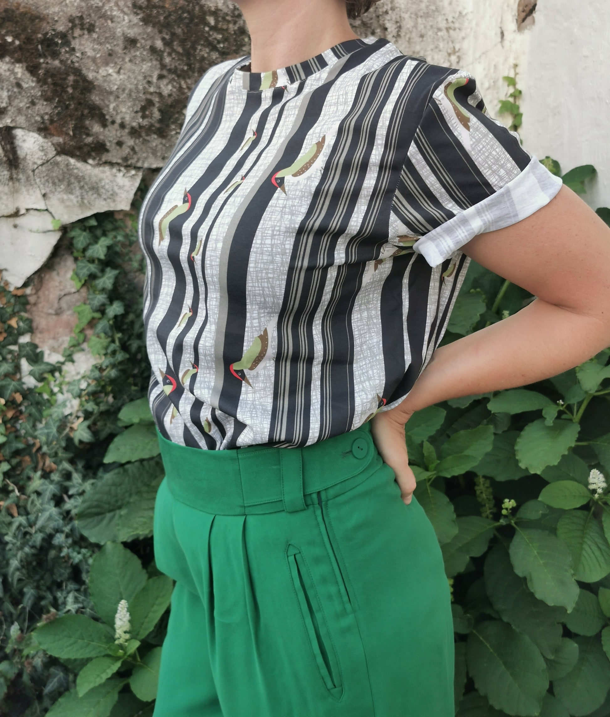 T-Shirt aus Biobaumwolle mit Streifenmuster in unregelmäßigen Abständen- die Streifen sind schwarz auf weiß und ein Grünspecht pickt Löcher in die Streifen, witzig, verspielt.