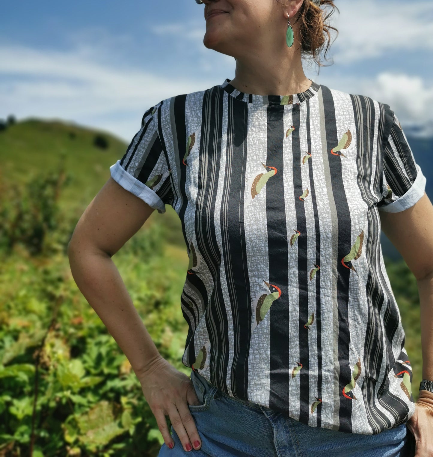 T-Shirt aus Biobaumwolle mit Streifenmuster in unregelmäßigen Abständen- die Streifen sind schwarz auf weiß und ein Grünspecht pickt Löcher in die Streifen, witzig, verspielt.