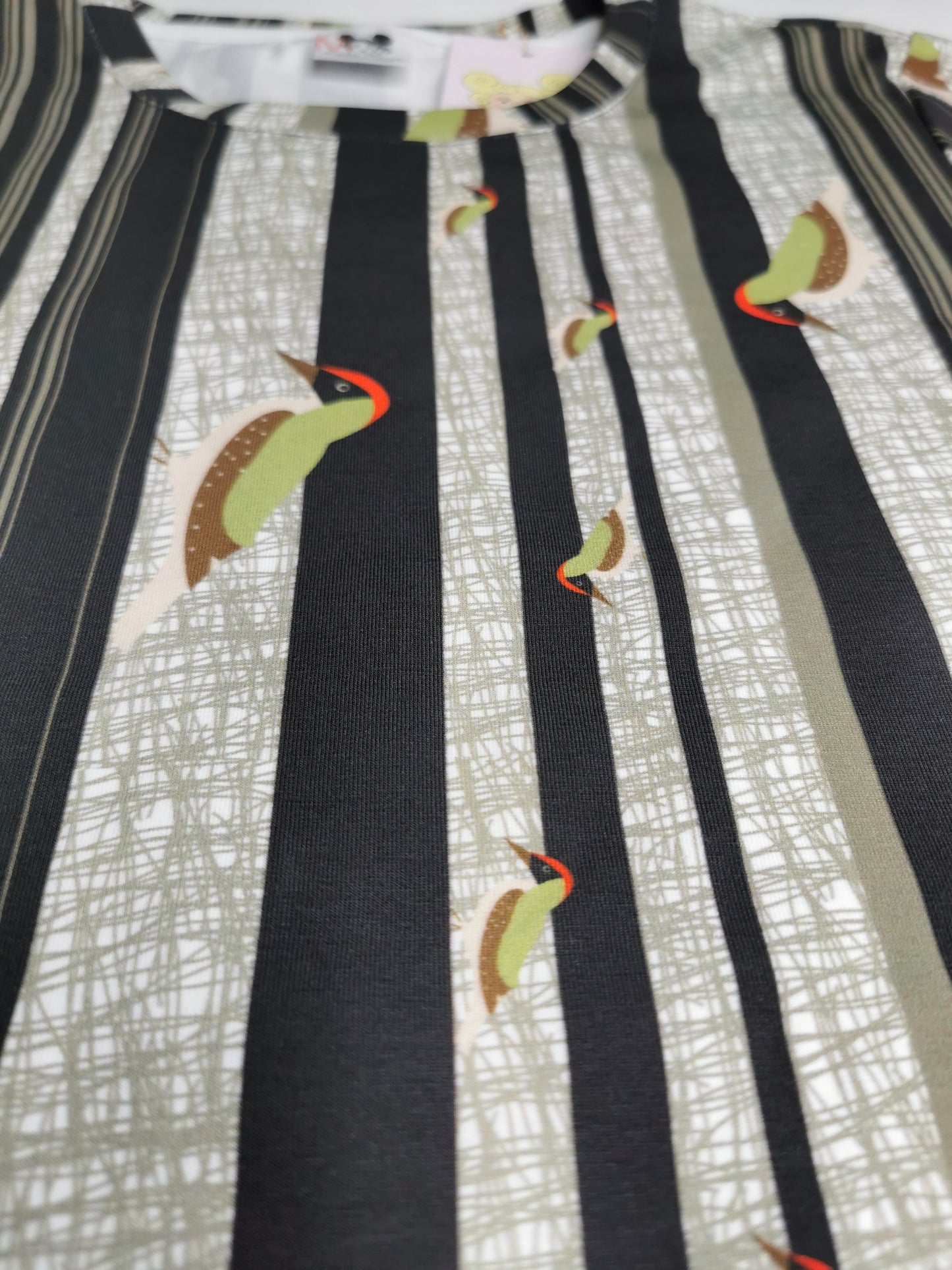 T-Shirt aus Biobaumwolle mit Streifenmuster in unregelmäßigen Abständen- die Streifen sind schwarz auf weiß und ein Grünspecht pickt Löcher in die Streifen, witzig, verspielt.