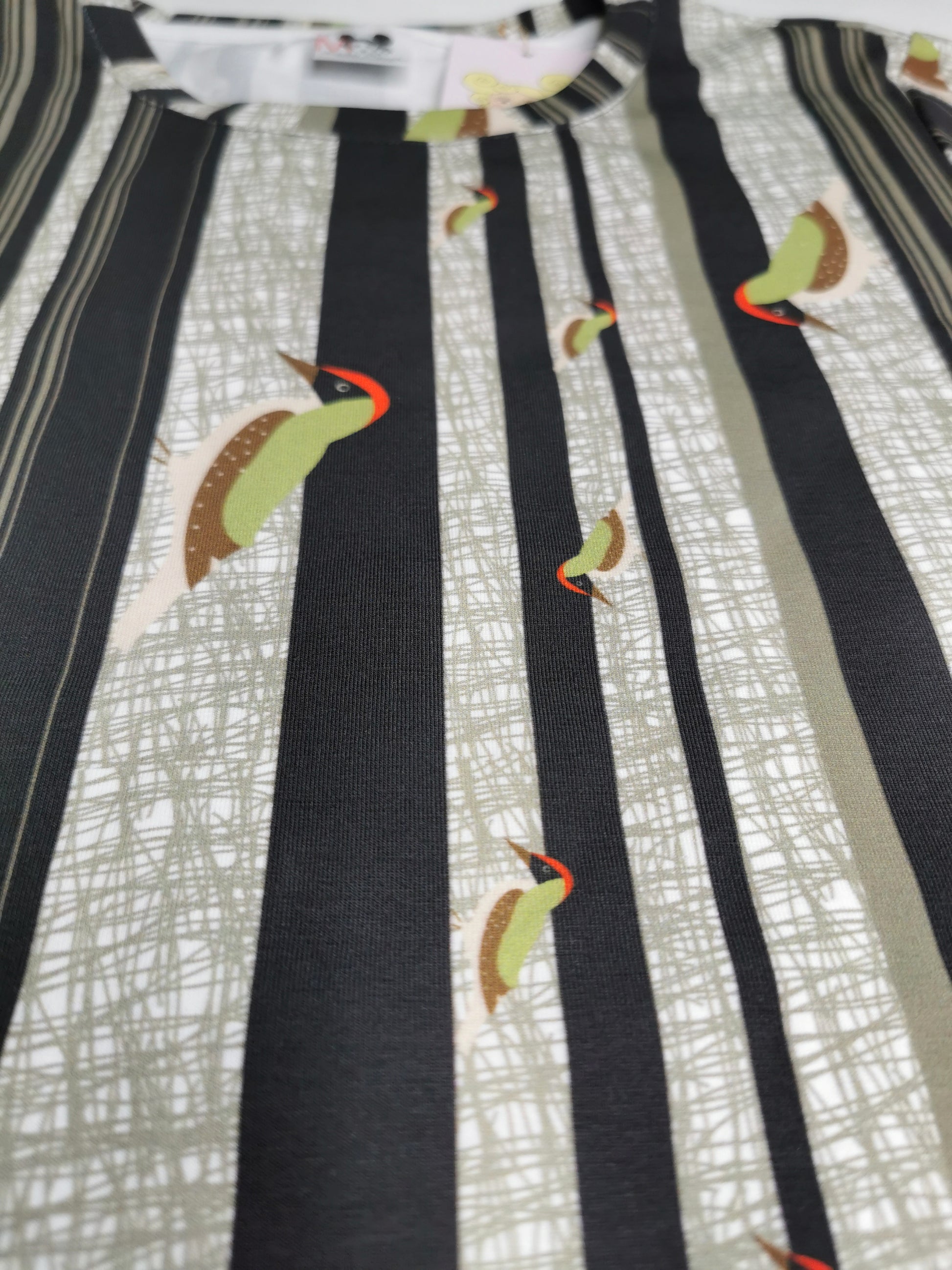 T-Shirt aus Biobaumwolle mit Streifenmuster in unregelmäßigen Abständen- die Streifen sind schwarz auf weiß und ein Grünspecht pickt Löcher in die Streifen, witzig, verspielt.