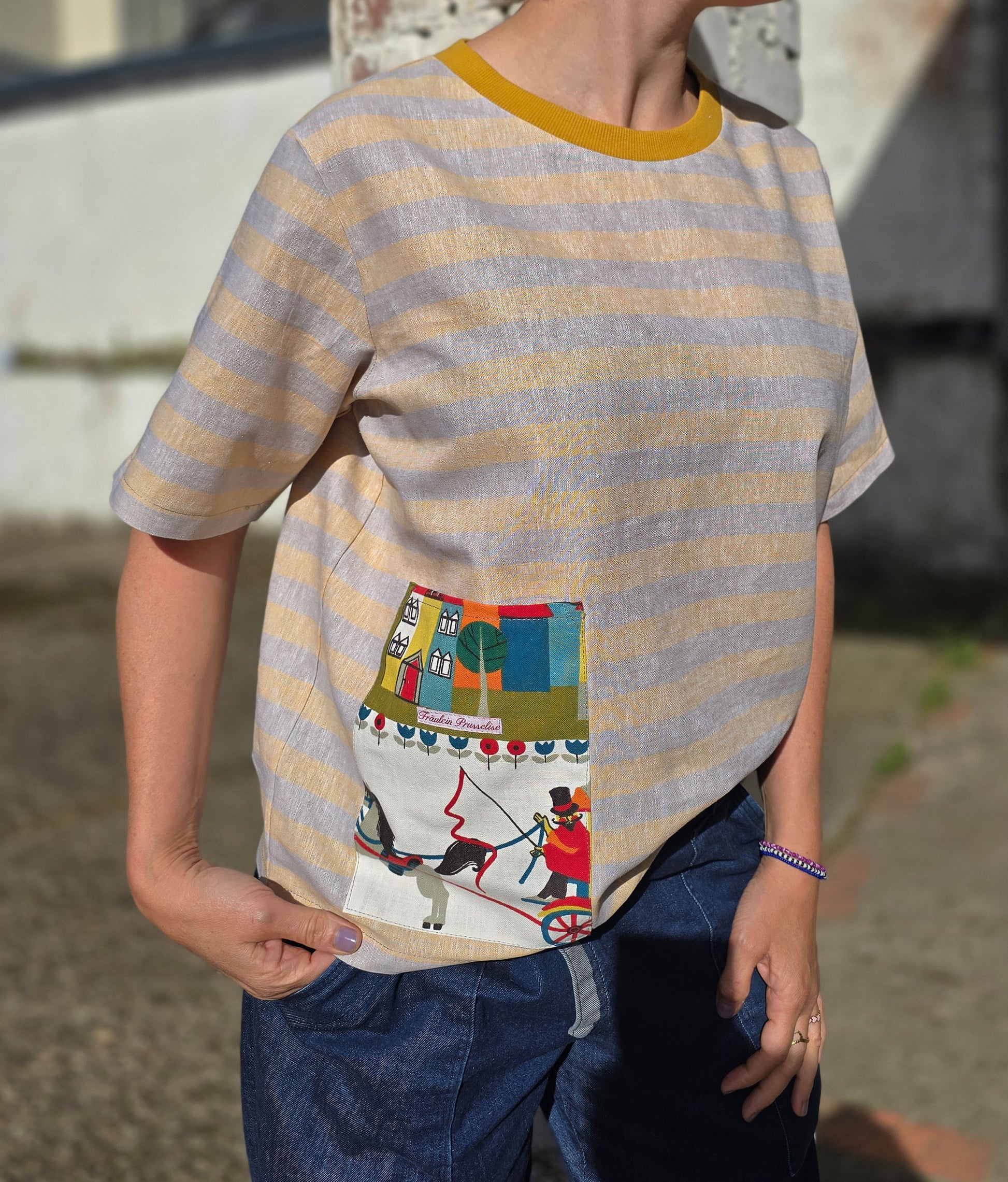 Loose Fit Shirt aus Leinen mit Baumwolle, Blockstreifen in Melange beige und gelb mit Aufsatztasche aus Landschafts Retrostoff mit Häuserzeile, Kutsche,Pferdchen,spielenden Menschen je nach Soffausschnitt.
