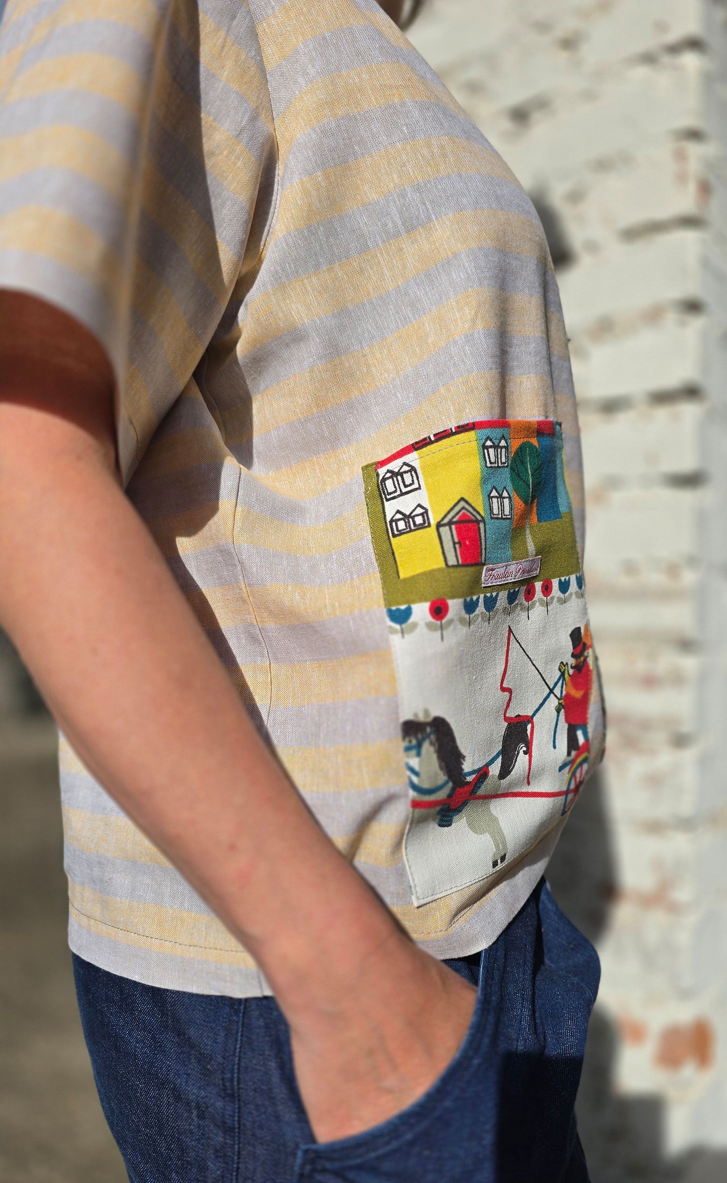 Loose Fit Shirt aus Leinen mit Baumwolle, Blockstreifen in Melange beige und gelb mit Aufsatztasche aus Landschafts Retrostoff mit Häuserzeile, Kutsche,Pferdchen,spielenden Menschen je nach Soffausschnitt.