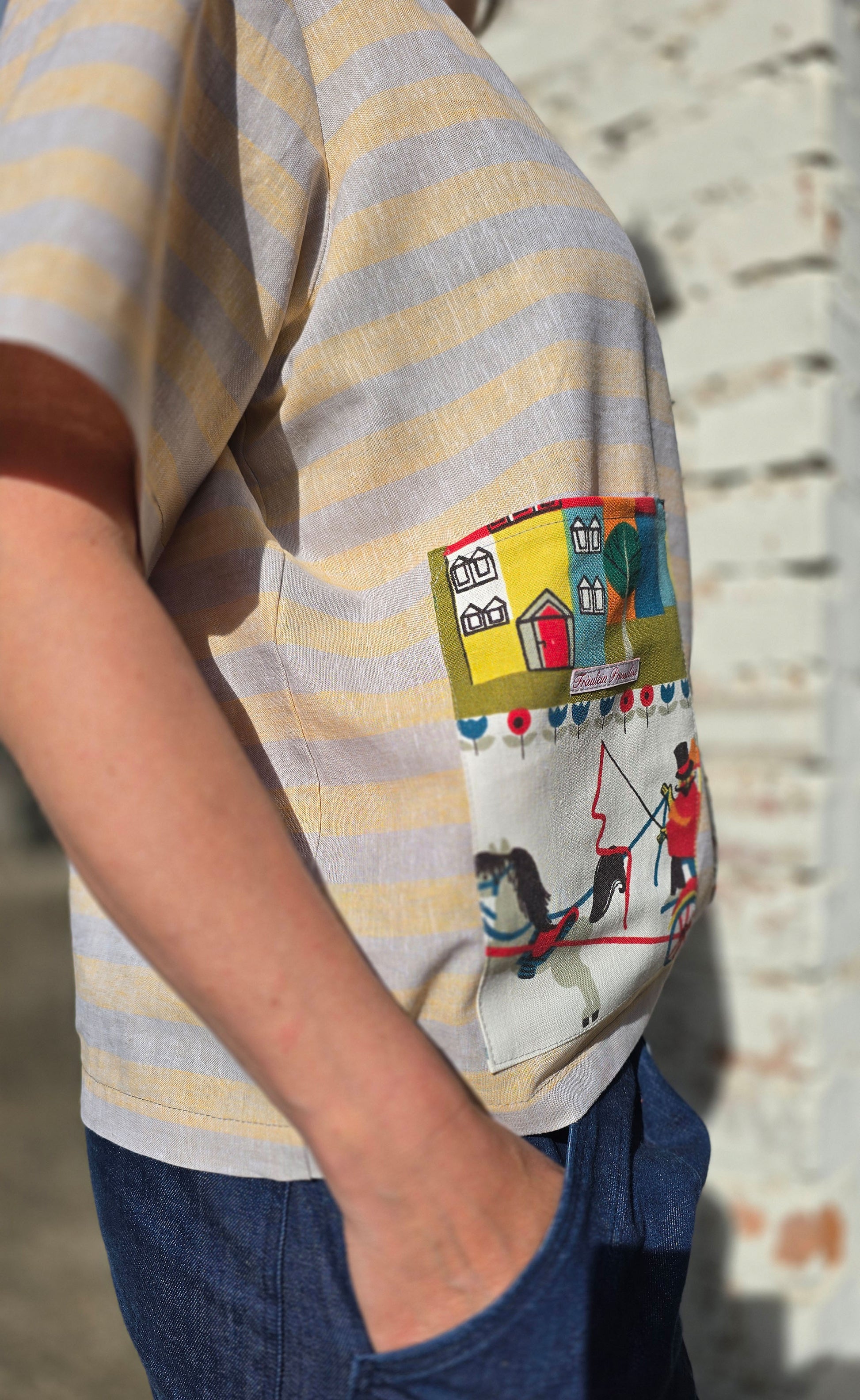 Loose Fit Shirt aus Leinen mit Baumwolle, Blockstreifen in Melange beige und gelb mit Aufsatztasche aus Landschafts Retrostoff mit Häuserzeile, Kutsche,Pferdchen,spielenden Menschen je nach Soffausschnitt.