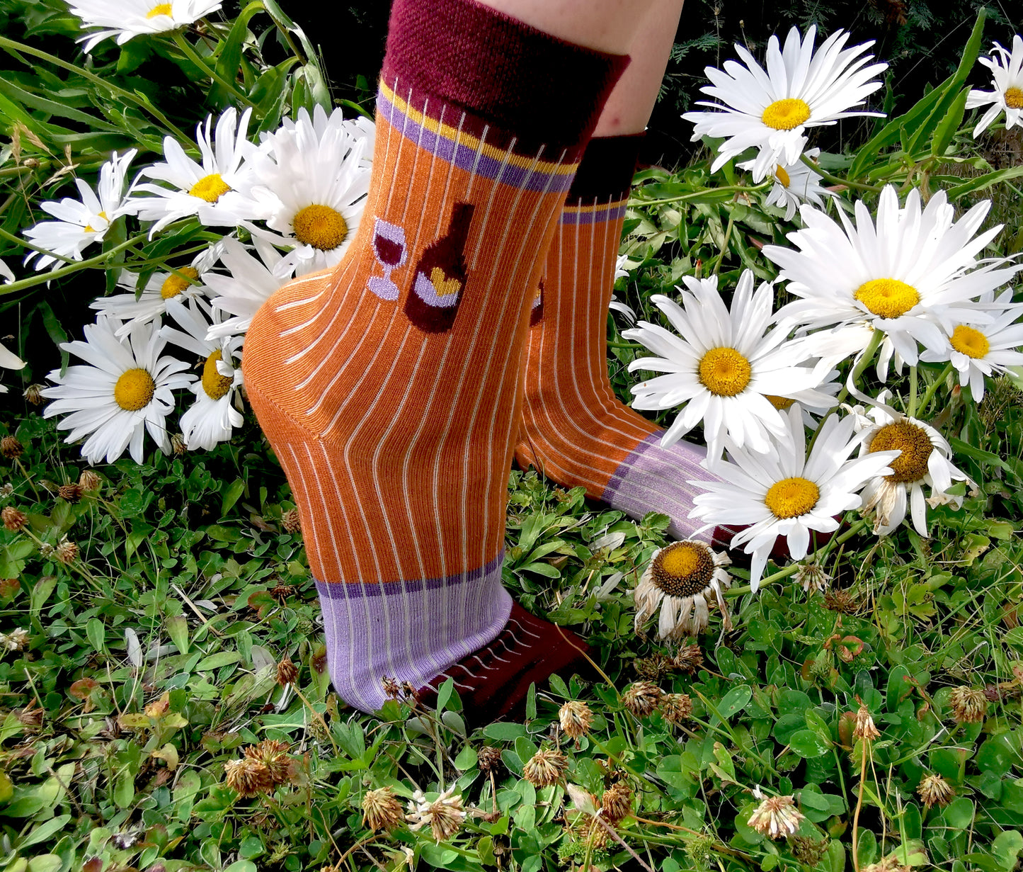 Wein Flasche un Glas auf einer zimt farbenen Socke in Ripp Strick mit colourblock Akzenten in bordeau, lila und gelb.