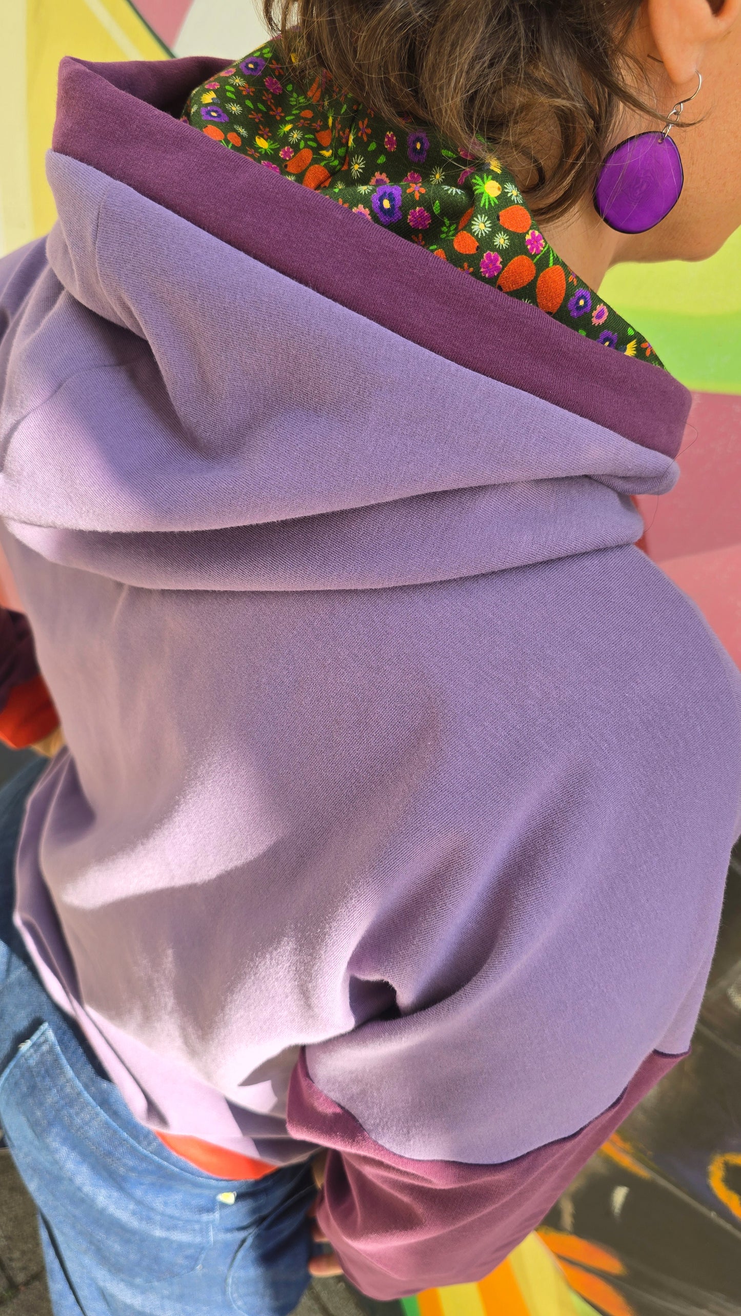 Hoody im Colourblock Design mit orange Bündchen, lila Ärmeln und in der lila Kapuze ist Millefleurs Jersey verarbeitet.