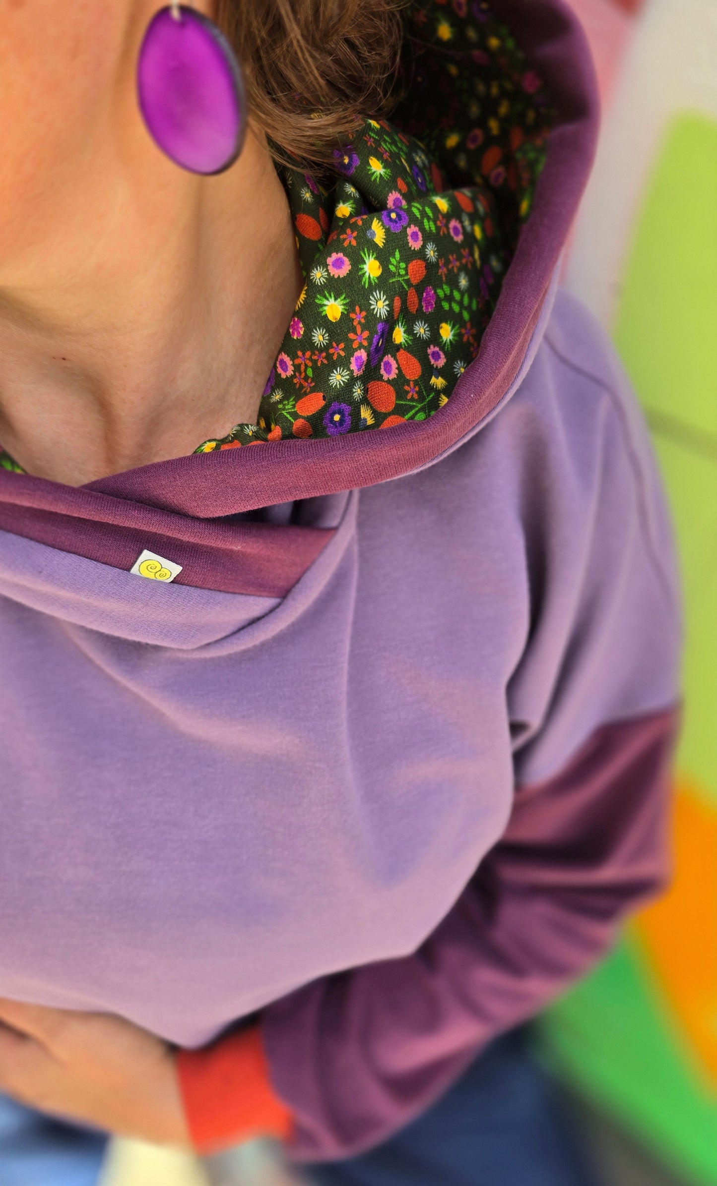 Hoody im Colourblock Design mit orange Bündchen, lila Ärmeln und in der lila Kapuze ist Millefleurs Jersey verarbeitet.