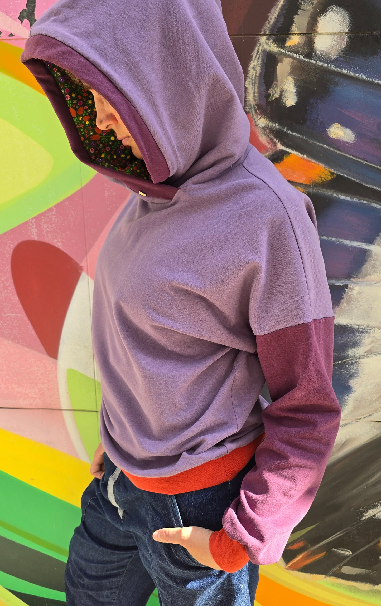 Hoody im Colourblock Design mit orange Bündchen, lila Ärmeln und in der lila Kapuze ist Millefleurs Jersey verarbeitet.