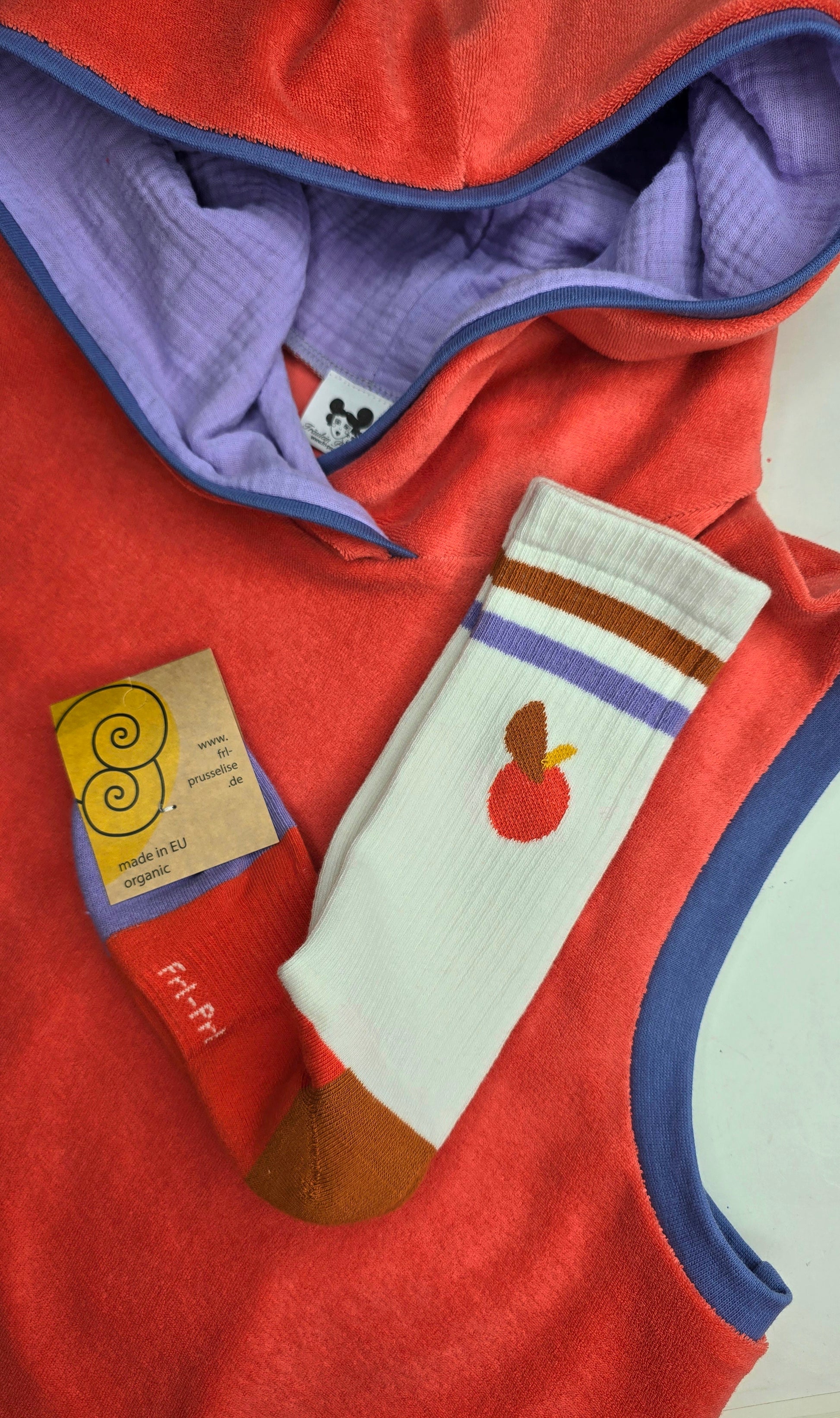 Locker sitzendes Top aus Frottee in knallrotorange, mit lila Farbakzenten an den Armausschnitten, die weiche Kapuze macht es Trendy und zeitlos trotz allem Retro Charme.