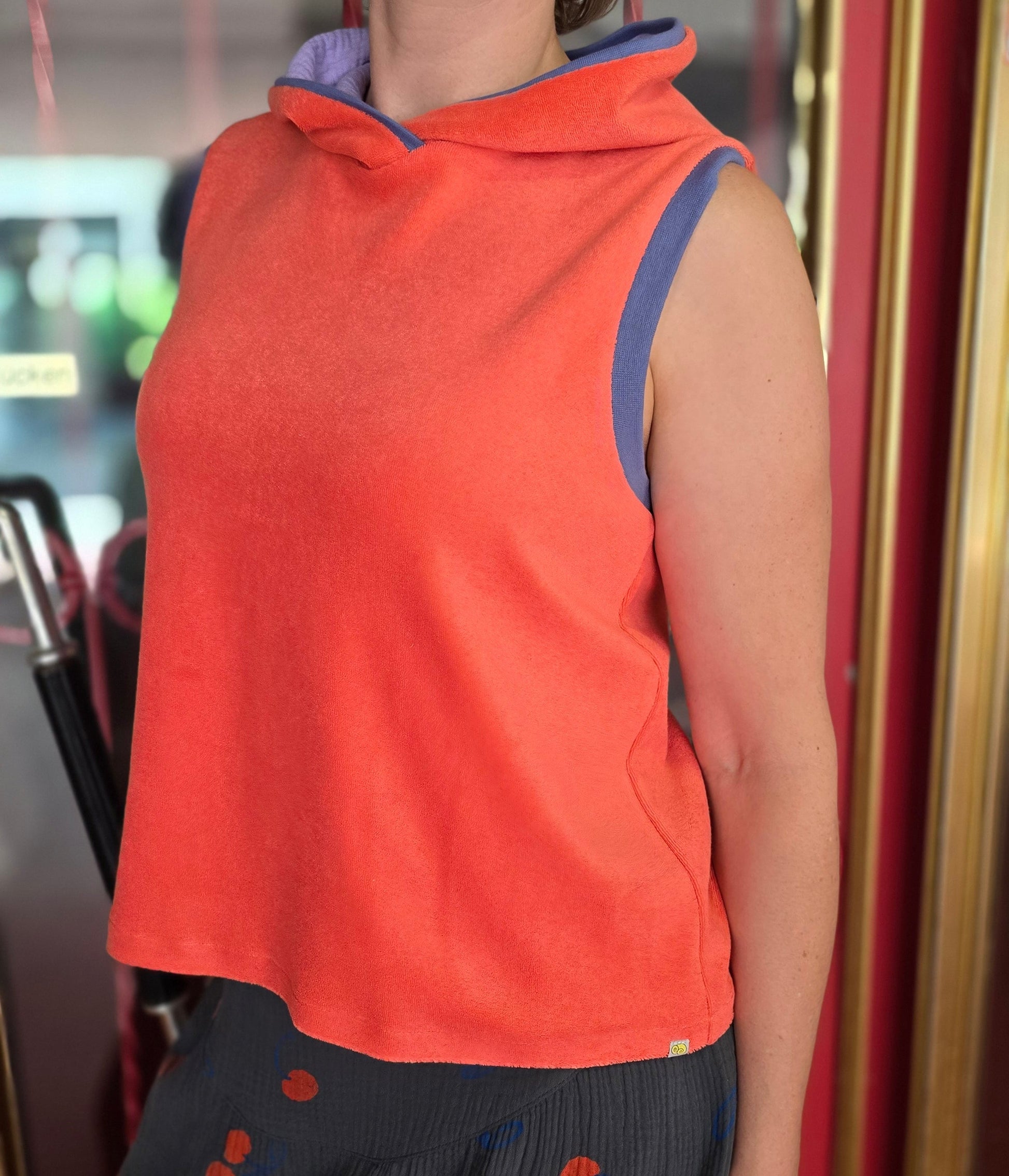 Locker sitzendes Top aus Frottee in knallrotorange, mit lila Farbakzenten an den Armausschnitten, die weiche Kapuze macht es Trendy und zeitlos trotz allem Retro Charme.