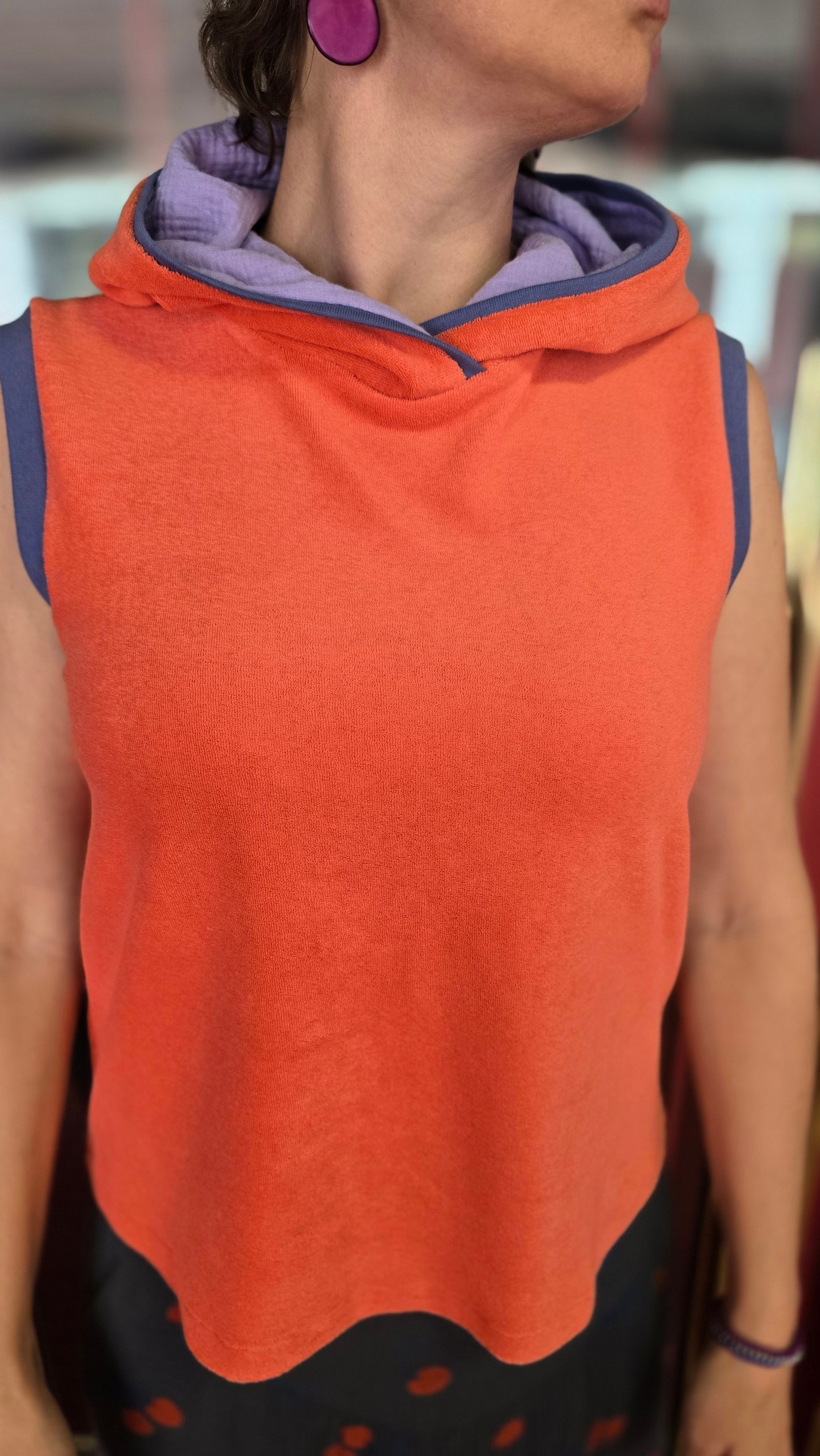 Locker sitzendes Top aus Frottee in knallrotorange, mit lila Farbakzenten an den Armausschnitten, die weiche Kapuze macht es Trendy und zeitlos trotz allem Retro Charme.