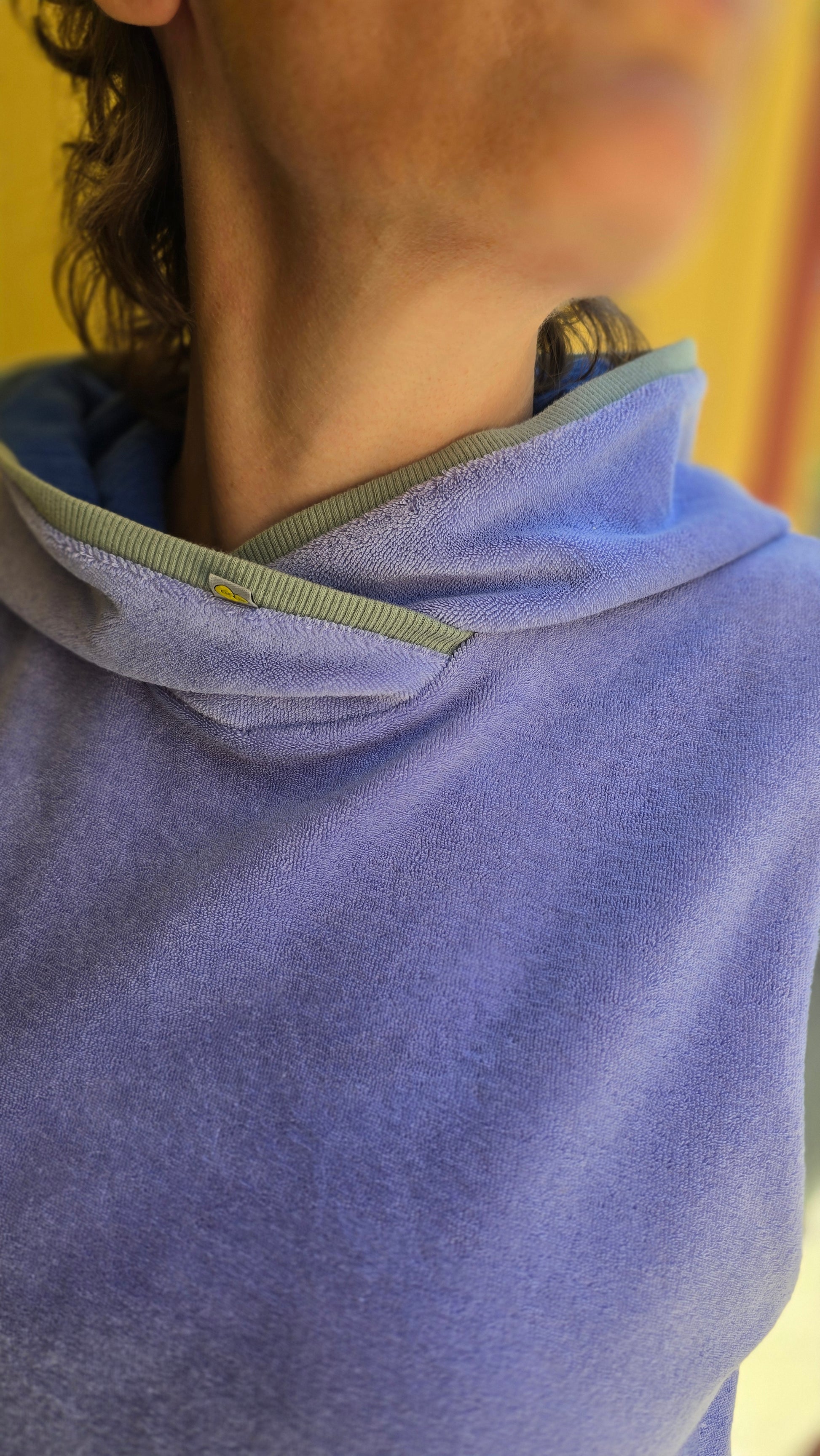 Locker sitzendes, kurzes Top aus Frottee in lila, mit salbei und königsblau Farbakzenten an den Armausschnitten, die weiche Kapuze macht es Trendy und zeitlos trotz eindeutigem Retro Charme.