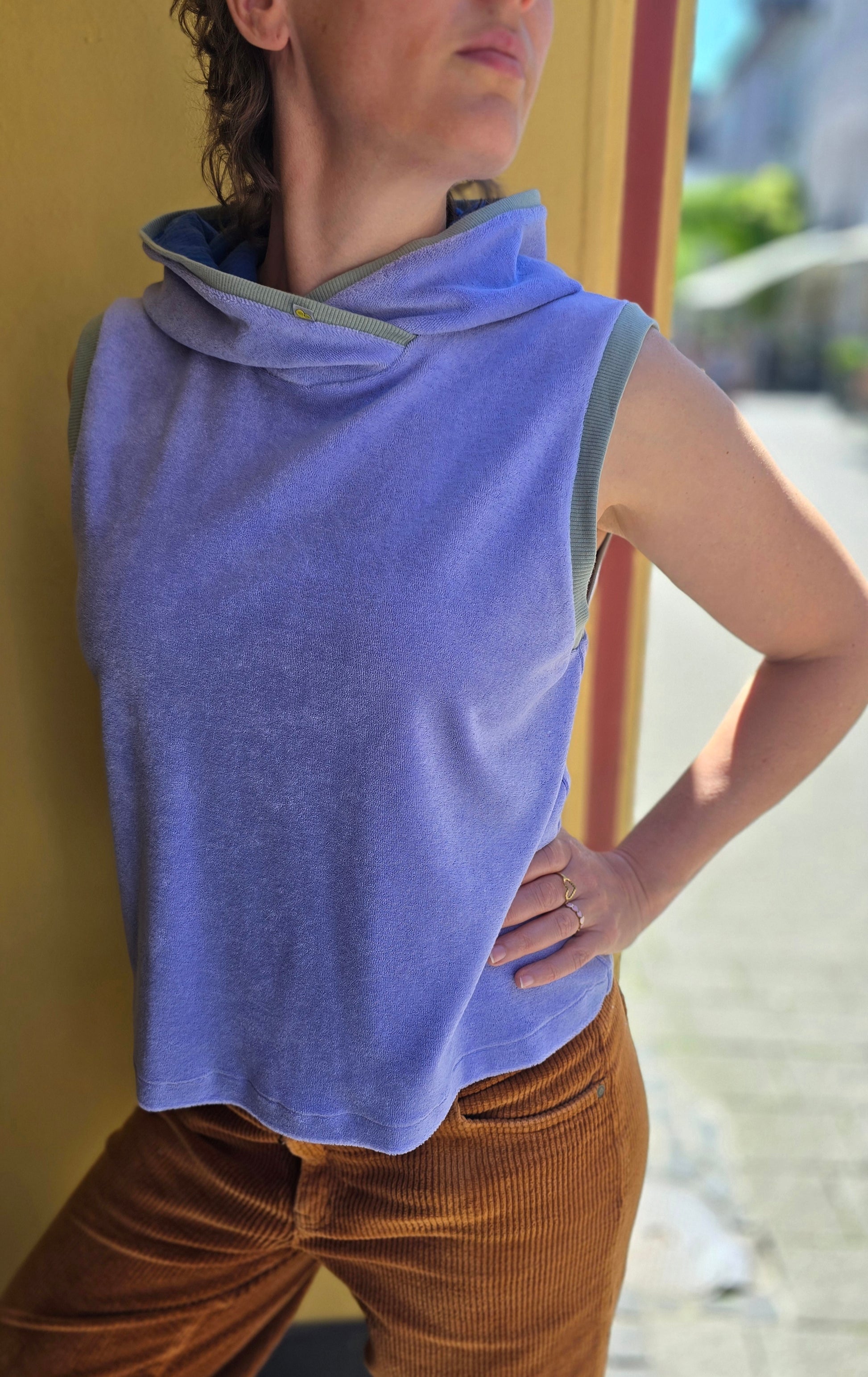 Locker sitzendes, kurzes Top aus Frottee in lila, mit salbei und königsblau Farbakzenten an den Armausschnitten, die weiche Kapuze macht es Trendy und zeitlos trotz eindeutigem Retro Charme.