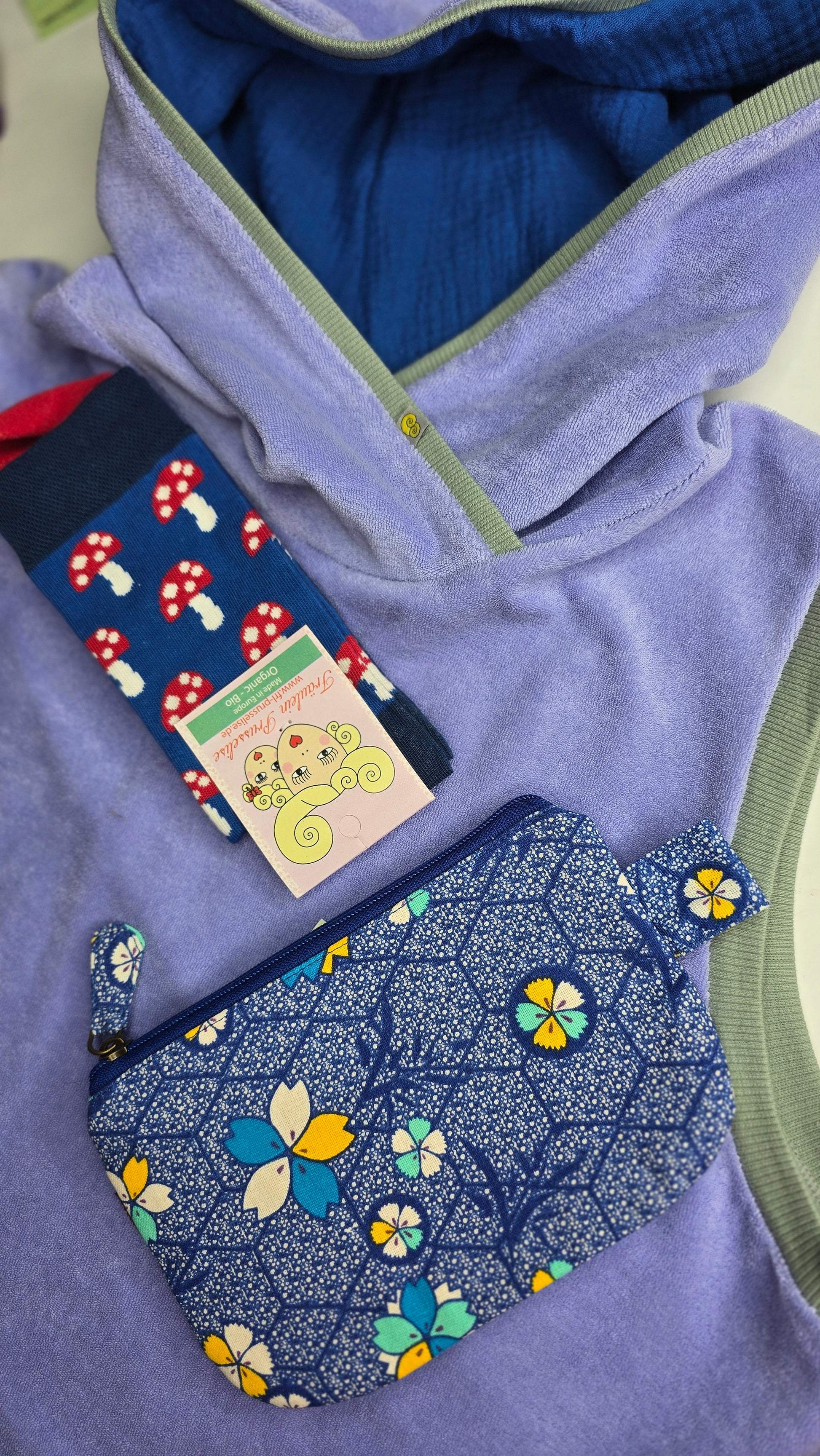 Locker sitzendes, kurzes Top aus Frottee in lila, mit salbei und königsblau Farbakzenten an den Armausschnitten, die weiche Kapuze macht es Trendy und zeitlos trotz eindeutigem Retro Charme.