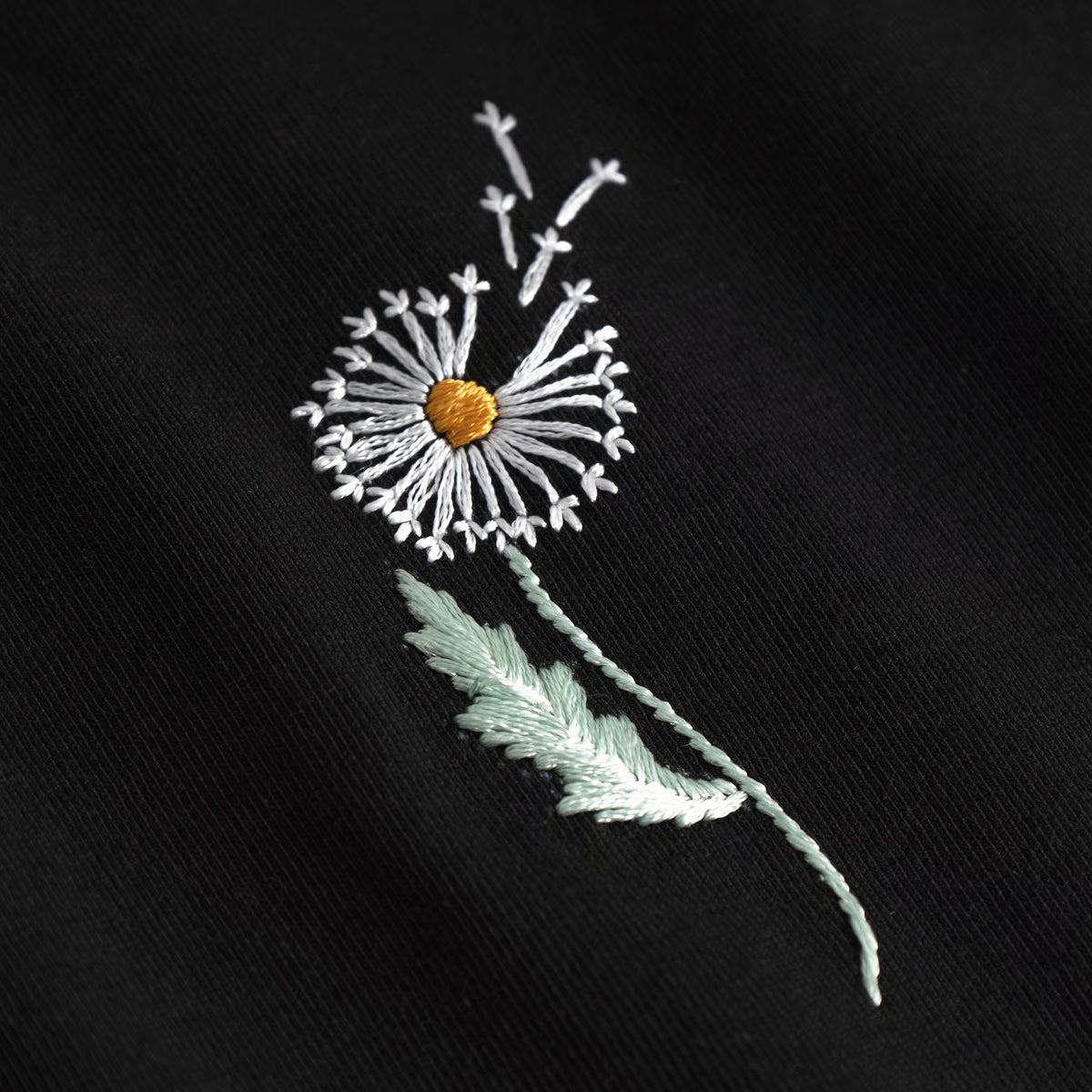 Schwarzes Damen T-Shirt mit gestickter Pusteblume im Brustbereich.
