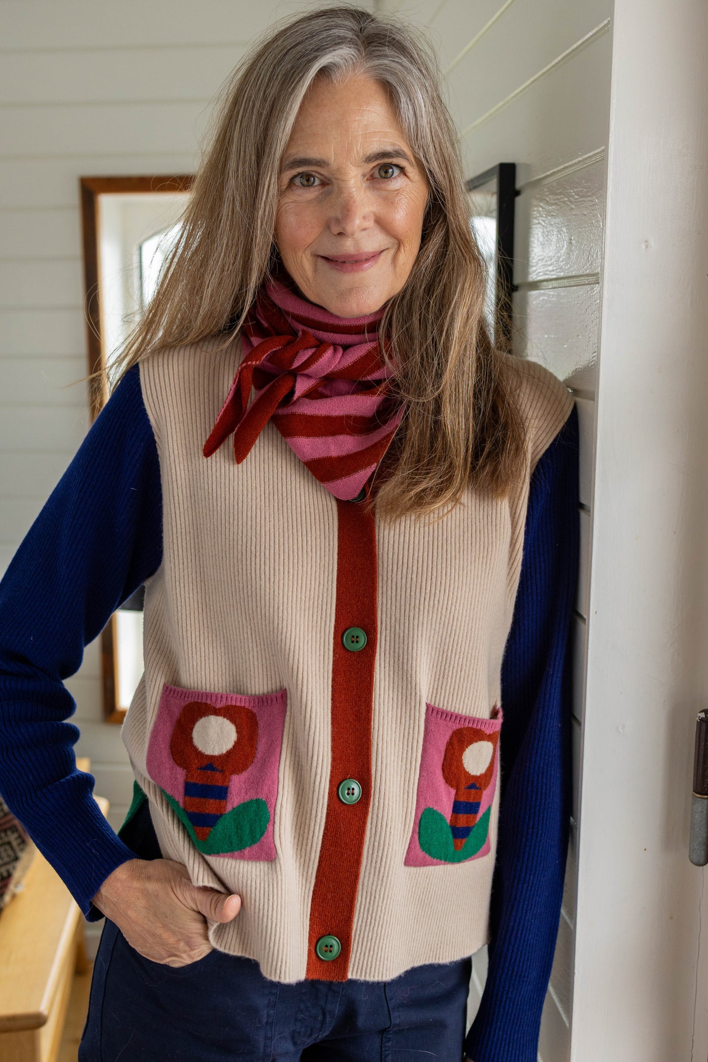 Kassischer, geknöpfter Cardigan mit V-Ausschnitt im Colourblock mit blau Ärmeln, grün Rücken und cremeweiss Vorderteil, die kleinen Aufsatztaschen frontal sorgen dann in Pink mit Prilblume fürs Abrunden des herrlichen Retro Charme, Merinowolle sorgt für Wertigkeit dazu.