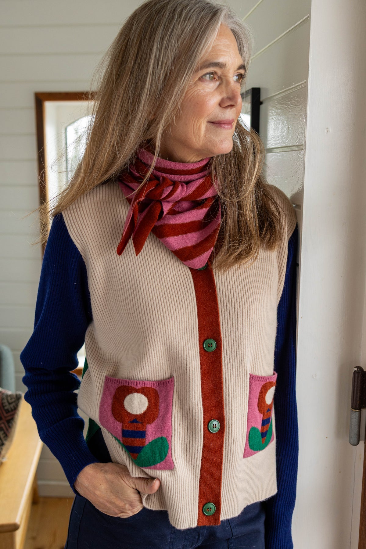 Kassischer, geknöpfter Cardigan mit V-Ausschnitt im Colourblock mit blau Ärmeln, grün Rücken und cremeweiss Vorderteil, die kleinen Aufsatztaschen frontal sorgen dann in Pink mit Prilblume fürs Abrunden des herrlichen Retro Charme, Merinowolle sorgt für Wertigkeit dazu.