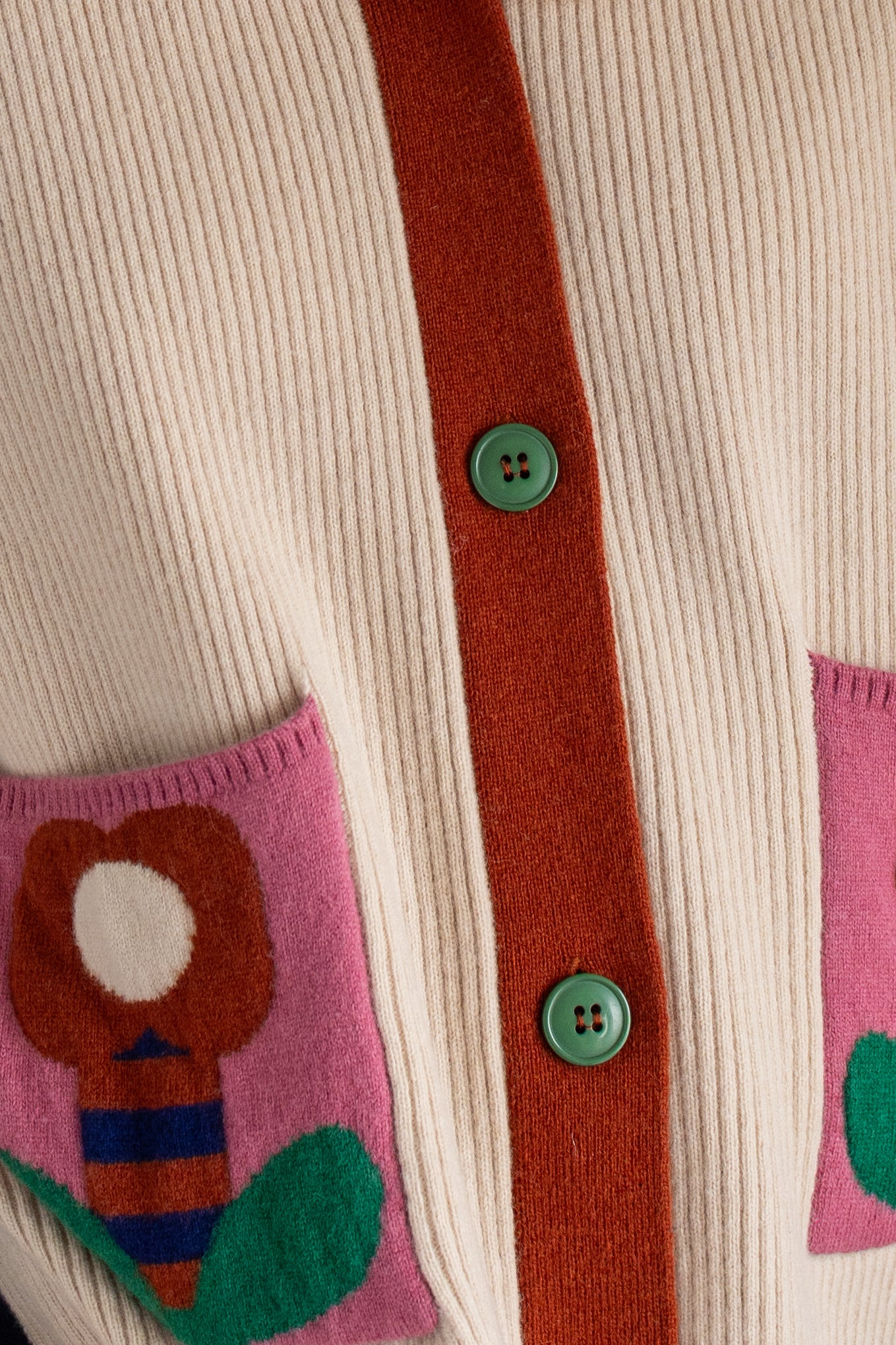 Kassischer, geknöpfter Cardigan mit V-Ausschnitt im Colourblock mit blau Ärmeln, grün Rücken und cremeweiss Vorderteil, die kleinen Aufsatztaschen frontal sorgen dann in Pink mit Prilblume fürs Abrunden des herrlichen Retro Charme, Merinowolle sorgt für Wertigkeit dazu.