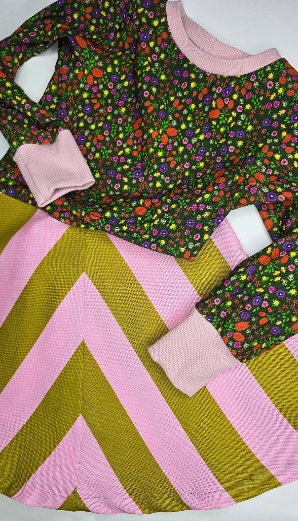 Kinderkleid mit Rockteil im Blockstreifen und Oberteil in multicolour Millefleurs, die Hauptfarben sind kiwi und rosa, lange Ärmel und rosa Bündchen.