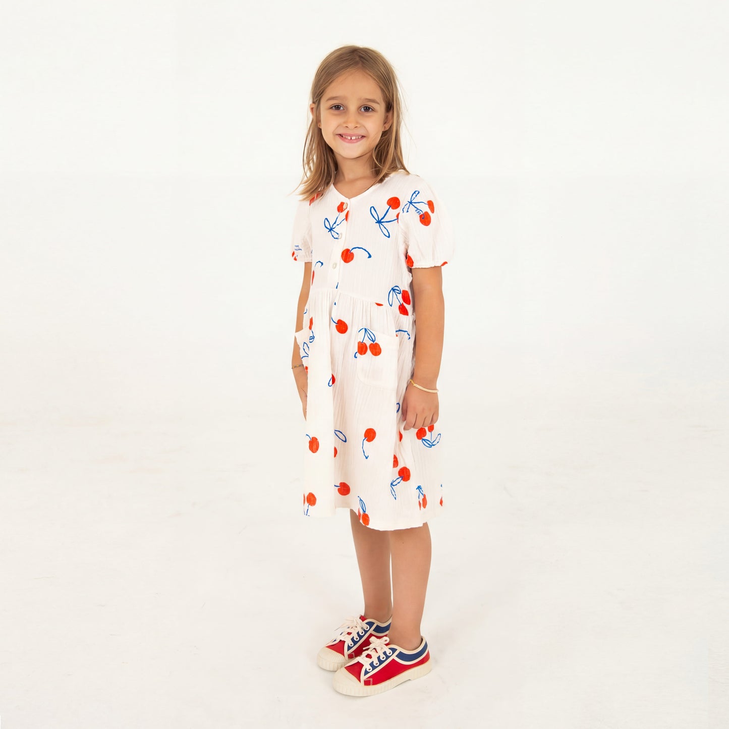 Kinderkleid in naturweiss Musselin mit aufgedruckten Kirschen, angekräuseltem Rockteil und kleinen Knöpfchen im Brustbereich, kurzer Ärmel. 