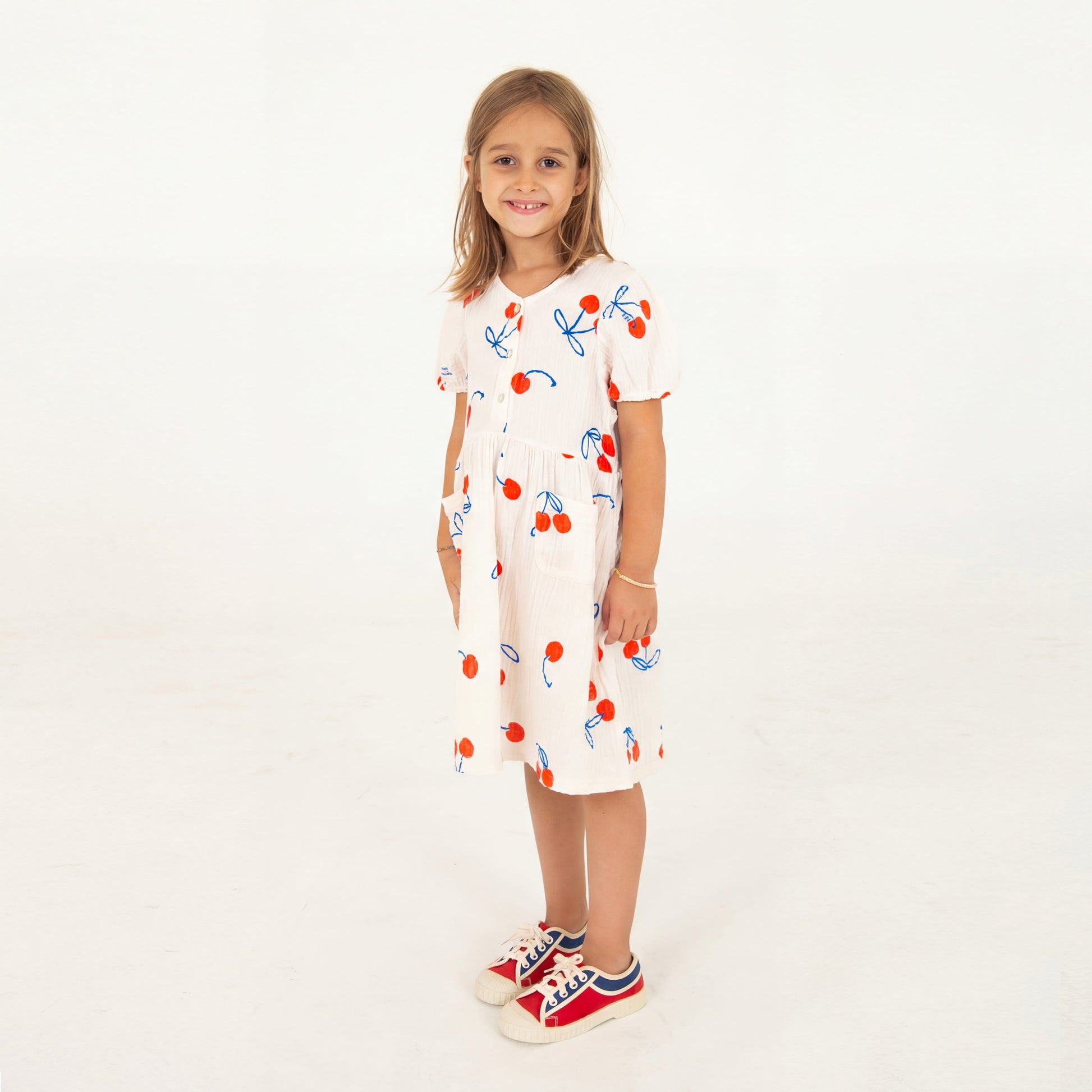 Kinderkleid in naturweiss Musselin mit aufgedruckten Kirschen, angekräuseltem Rockteil und kleinen Knöpfchen im Brustbereich, kurzer Ärmel. 