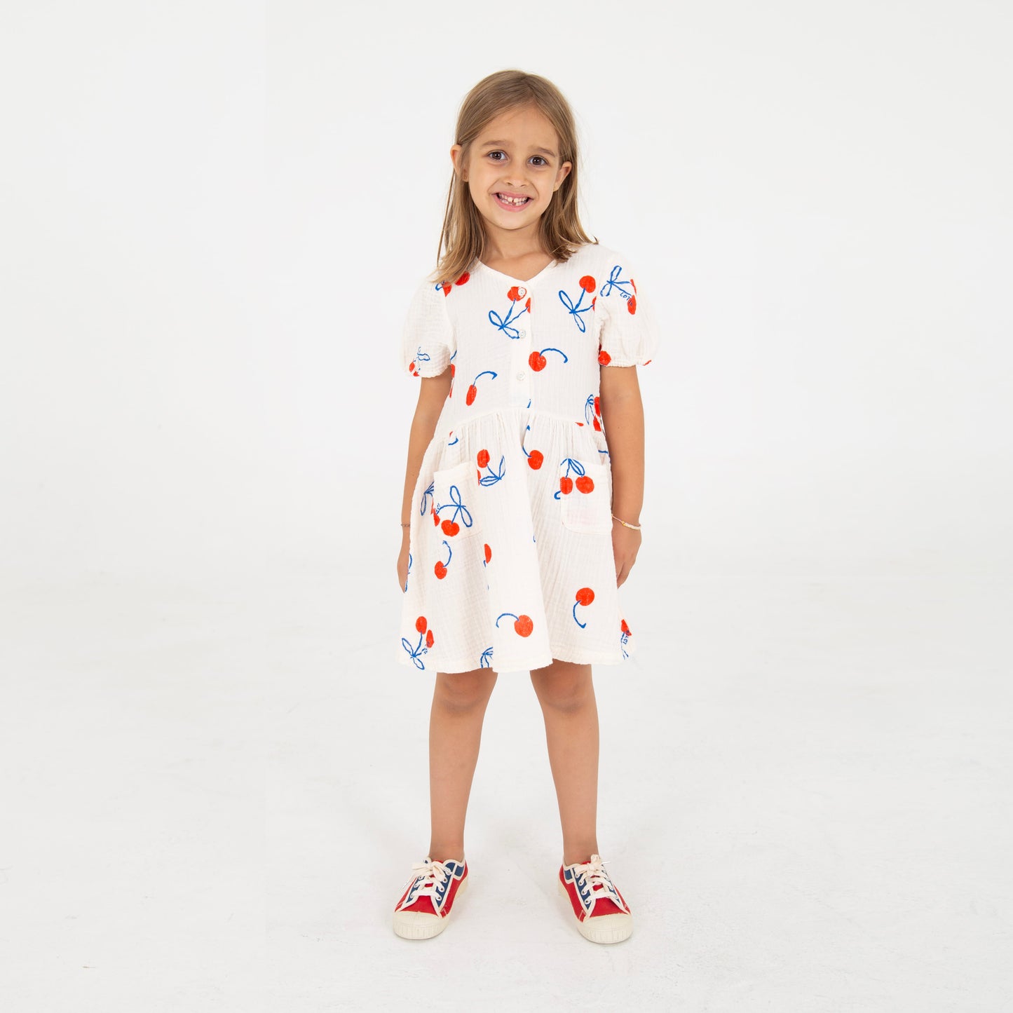 Kinderkleid in naturweiss Musselin mit aufgedruckten Kirschen, angekräuseltem Rockteil und kleinen Knöpfchen im Brustbereich, kurzer Ärmel. 