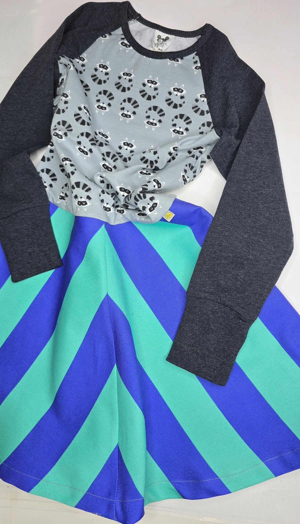 Kinderkleid mit gestreiftem Rockteil in türkis und blau mit angesetztem Oberteil mit Waschbärmister und dunkelgrauen Ärmeln.