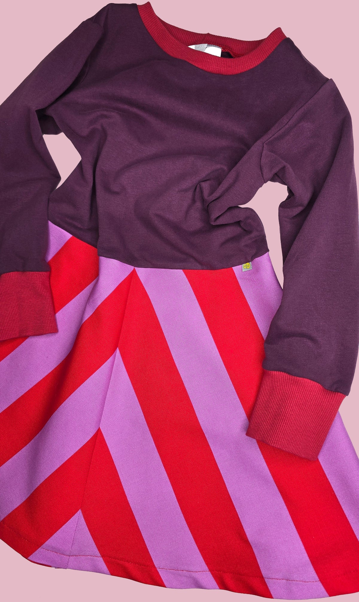 Kinderkleid mit gestreiftem Rockteil und einfarbigem Oberteil in lila, der Rck ist rot und lila gestreift.