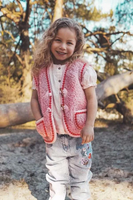 Weiche Kinderweste aus Teddyplüsch in reiner Wolle, pink mit roter Blumenbordüre als Akzent.