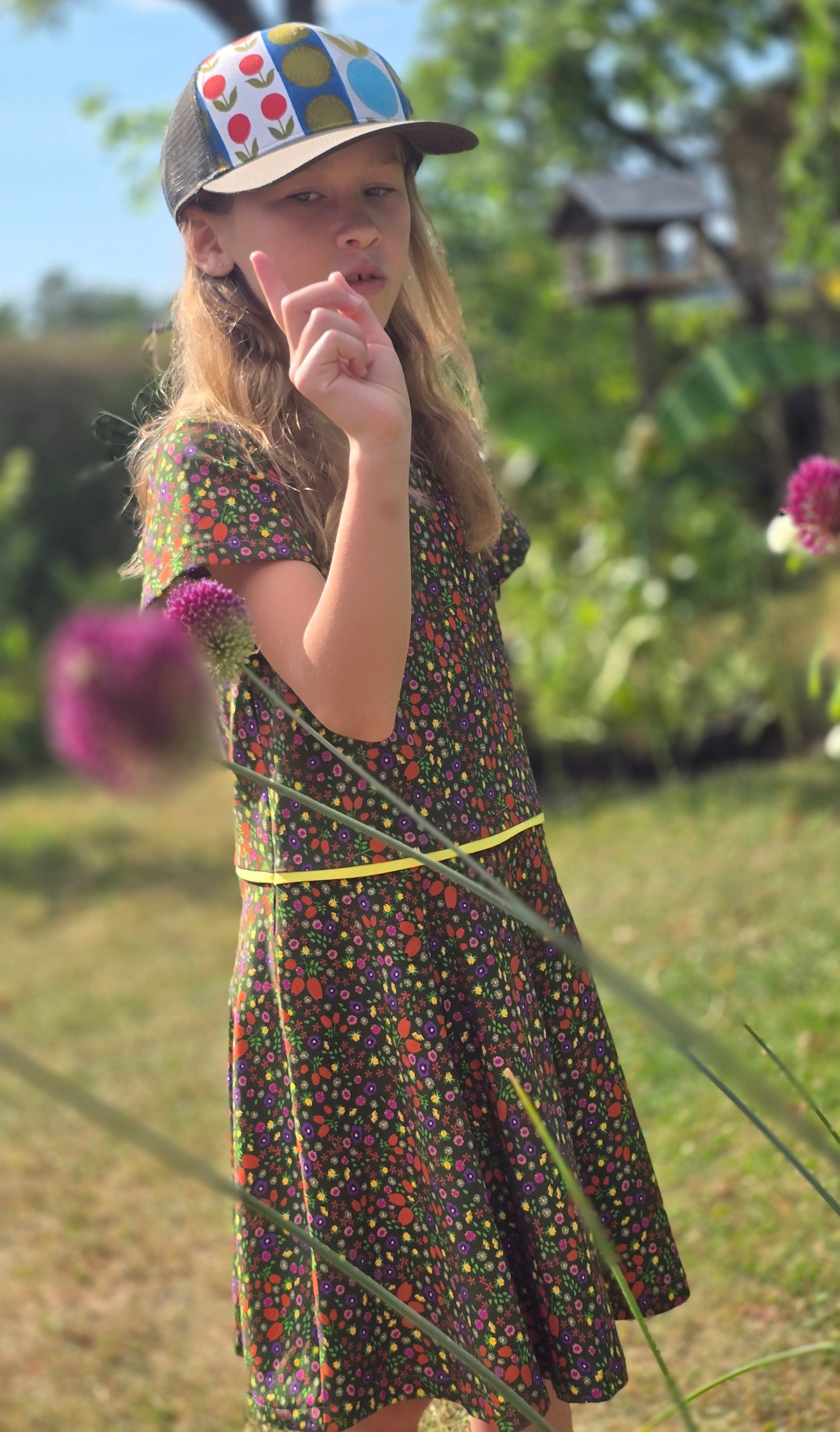 Ausgestelltes Kinderkleid mit Millefleur Muster in Oliv grundig, abgesetzt mit gelbem Kantenband kurzarm, verspielt.